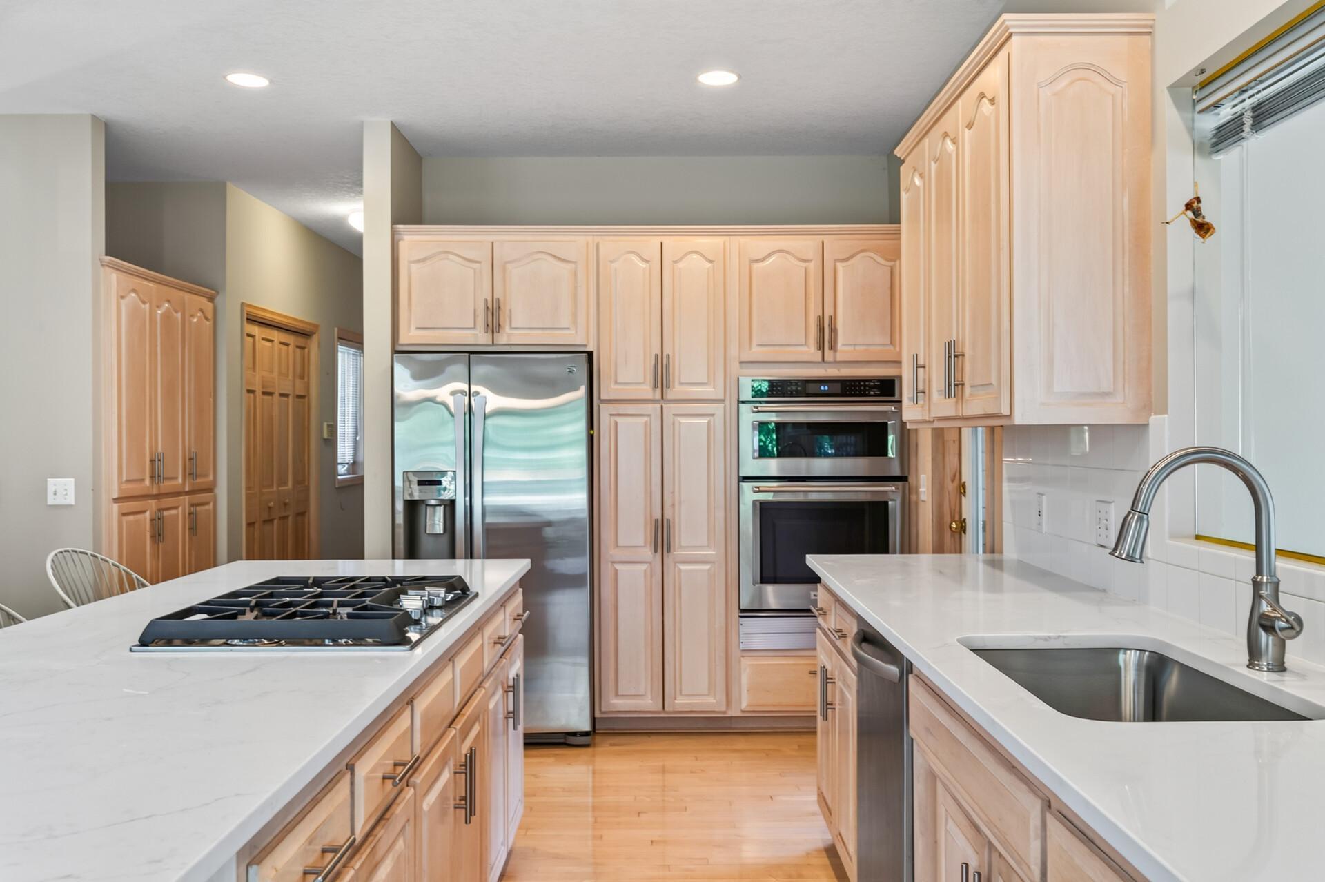 Kitchen with pale wood cabinets, white counters, a gas cooktop island, and stainless steel appliances.