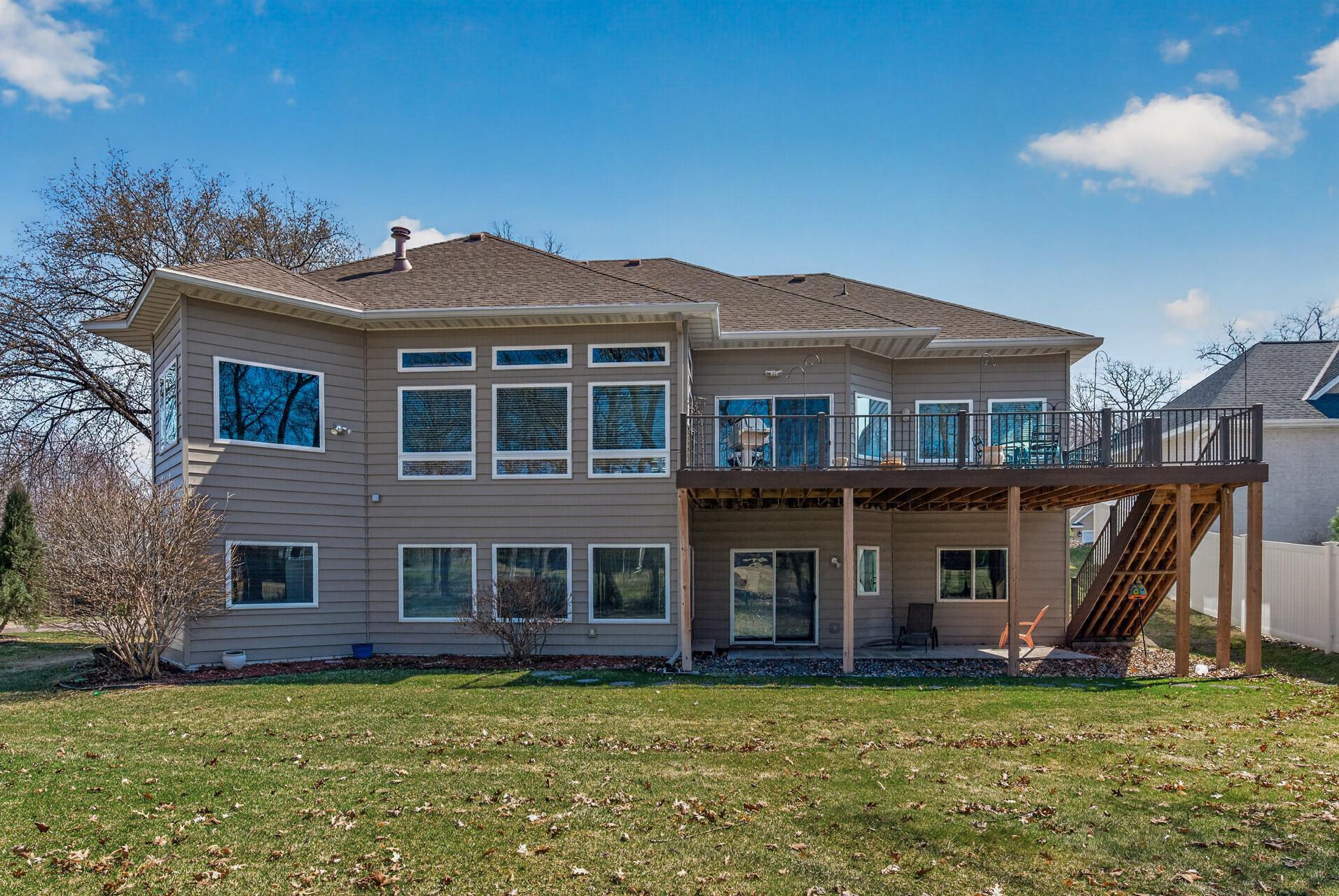 Rear of a gray two-story house with a raised deck and broad lawn.
