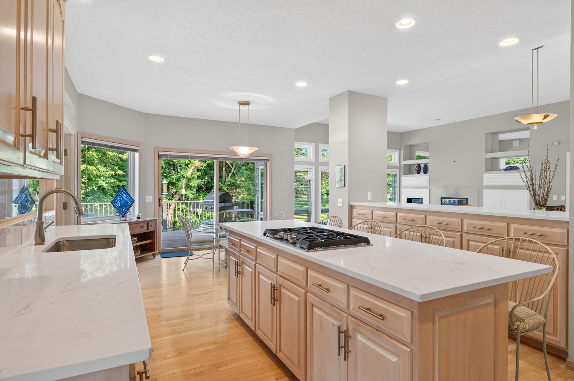 Open kitchen with a large cooktop island, light wood cabinets, and sliding doors to a green backyard.
