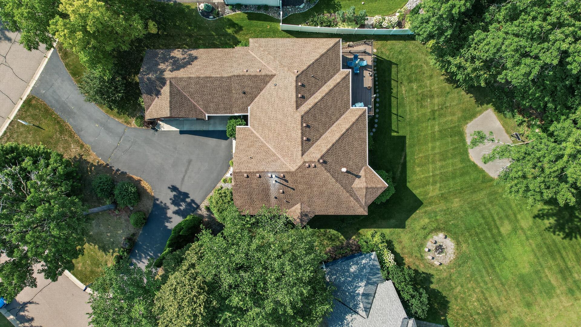 Aerial view of a home with a large brown roof, driveway, lawn, and backyard deck.