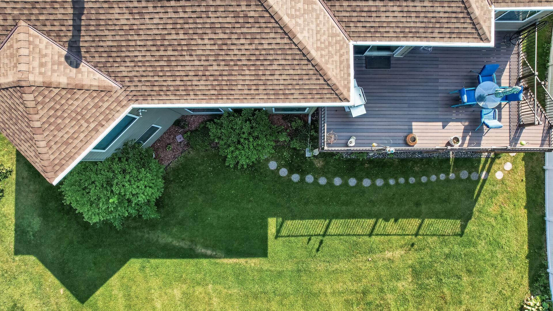 Aerial view of a landscaped backyard with a furnished deck and broad lawn.