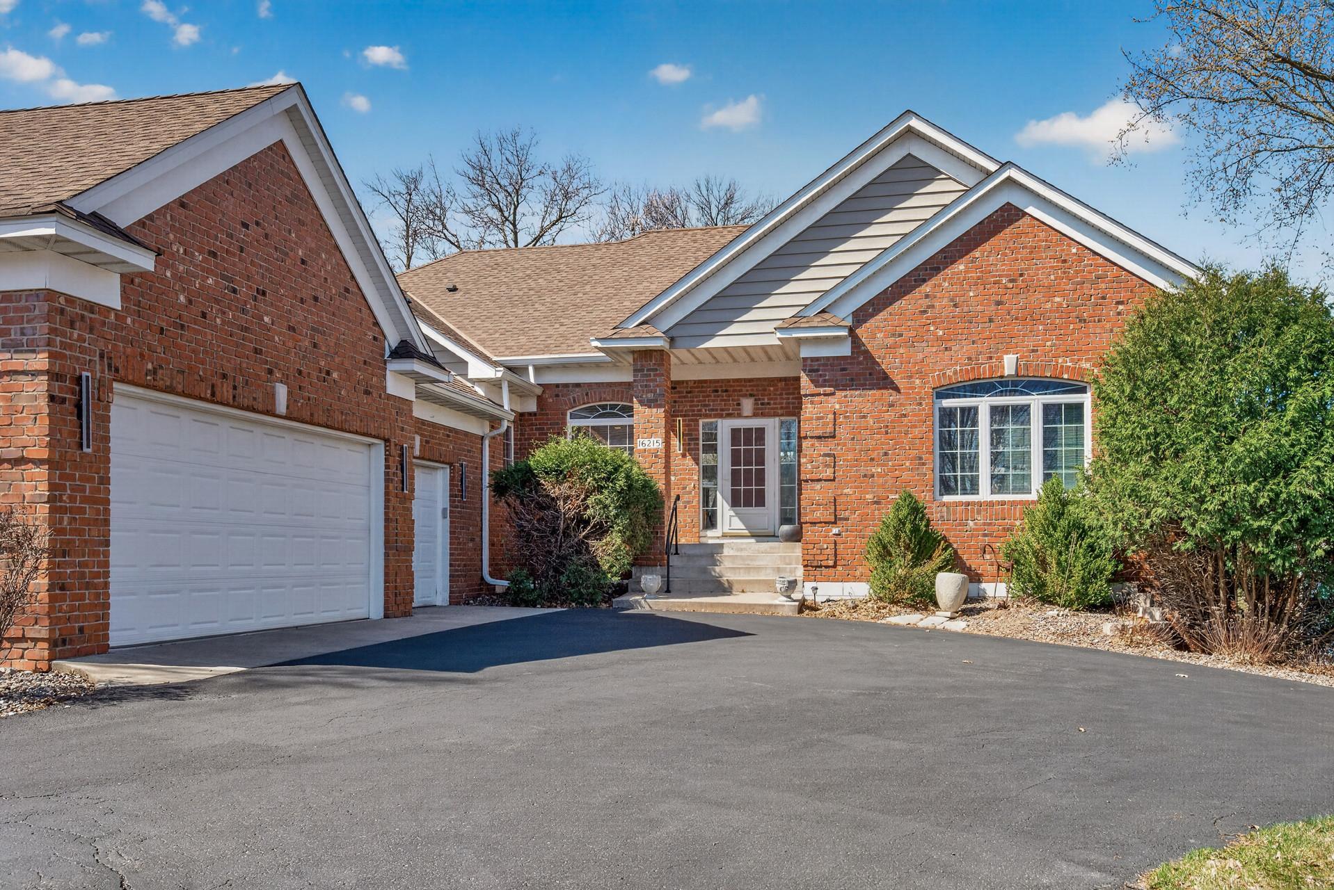 Red-brick home with an attached double garage, covered entry, and wide asphalt driveway.