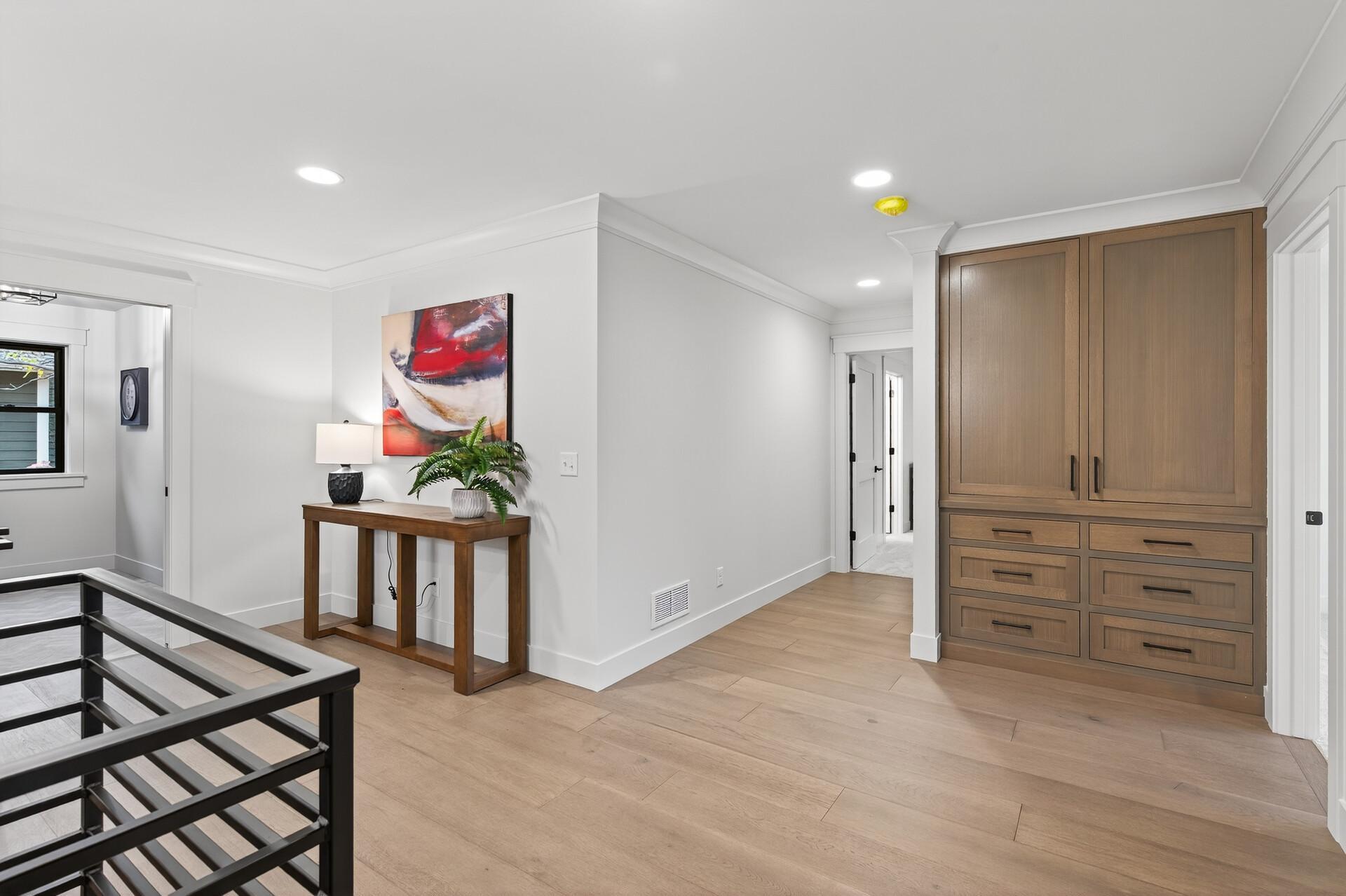 Hallway with built-in wood cabinetry, light flooring, and a black stair railing.