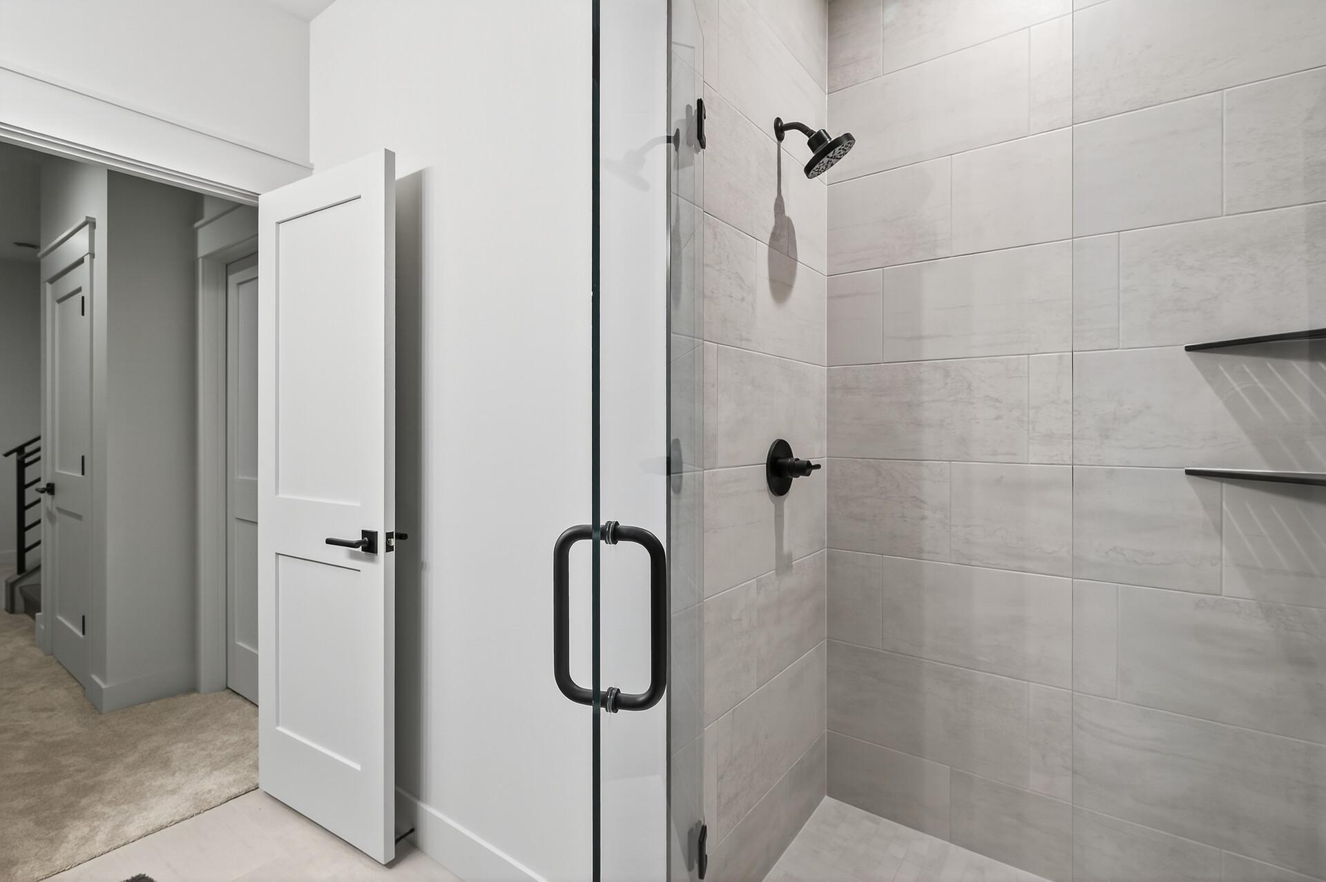 Bathroom with a tiled glass shower, matte-black fixtures, and built-in shelves.
