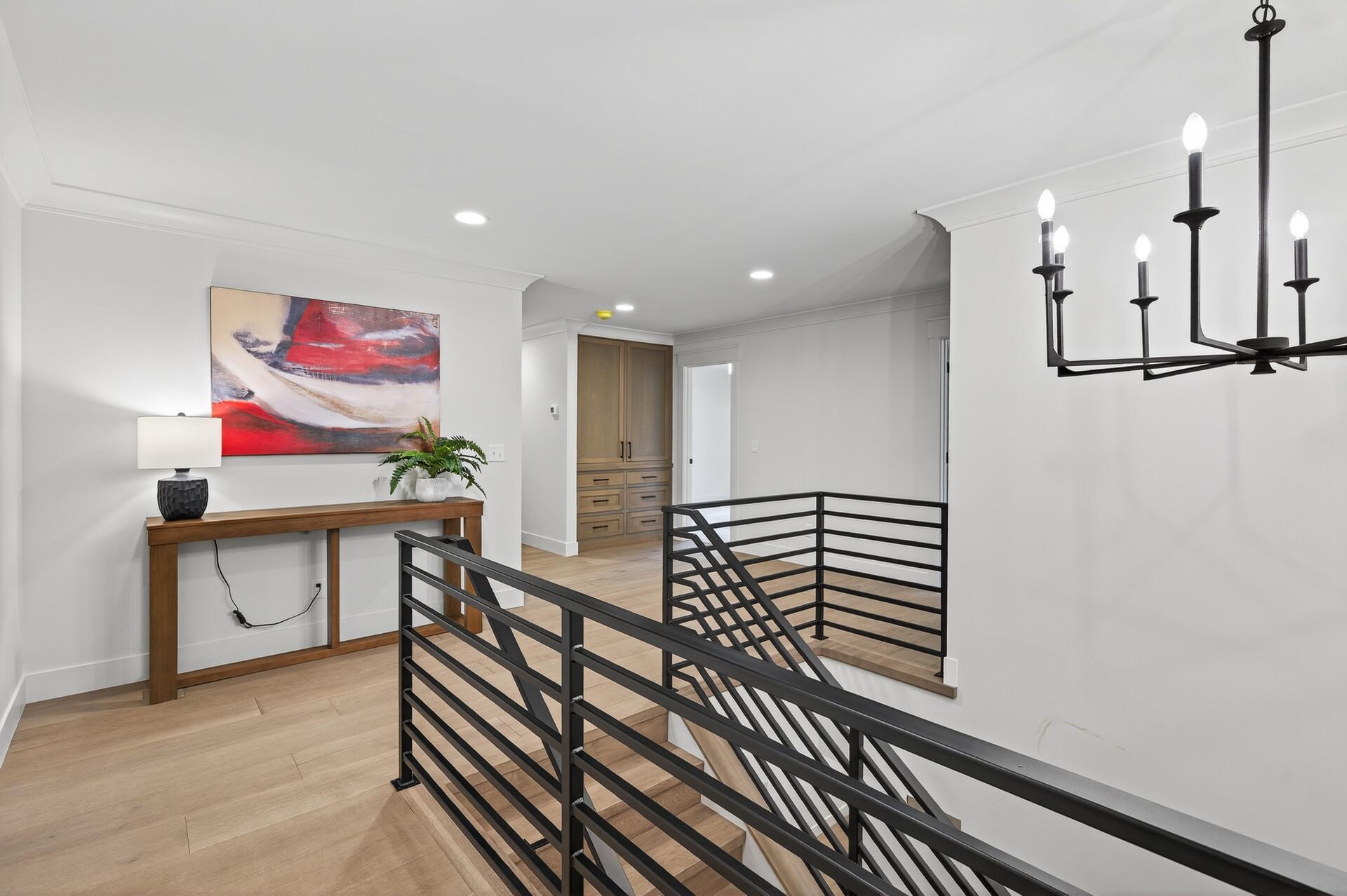 Upstairs landing with black metal stair railings, light wood floors, and a built-in cabinet.