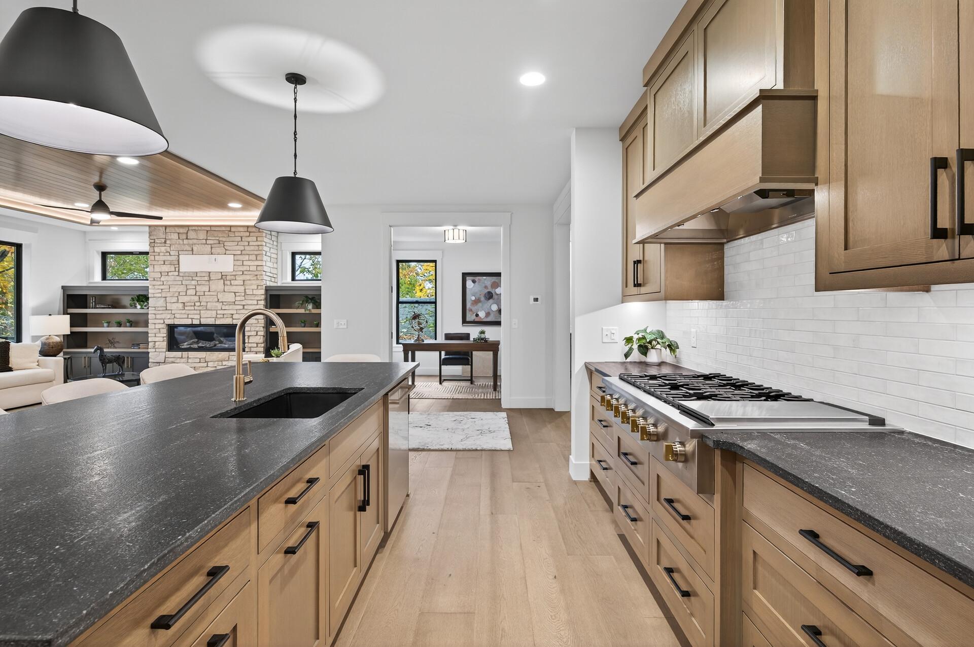 Kitchen with a dark stone island, light wood cabinets, brass faucet, and stainless gas range.