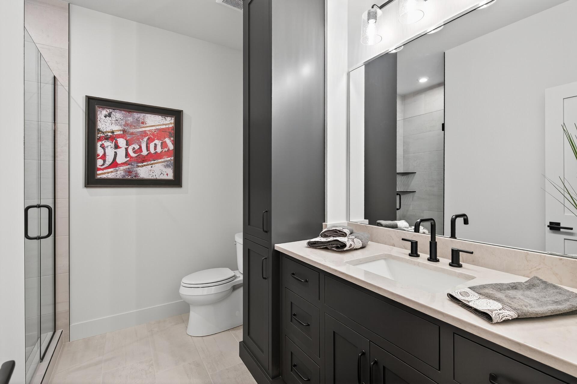 Modern bathroom with a glass shower, dark double vanity, pale stone counters, and framed red-and-white artwork.