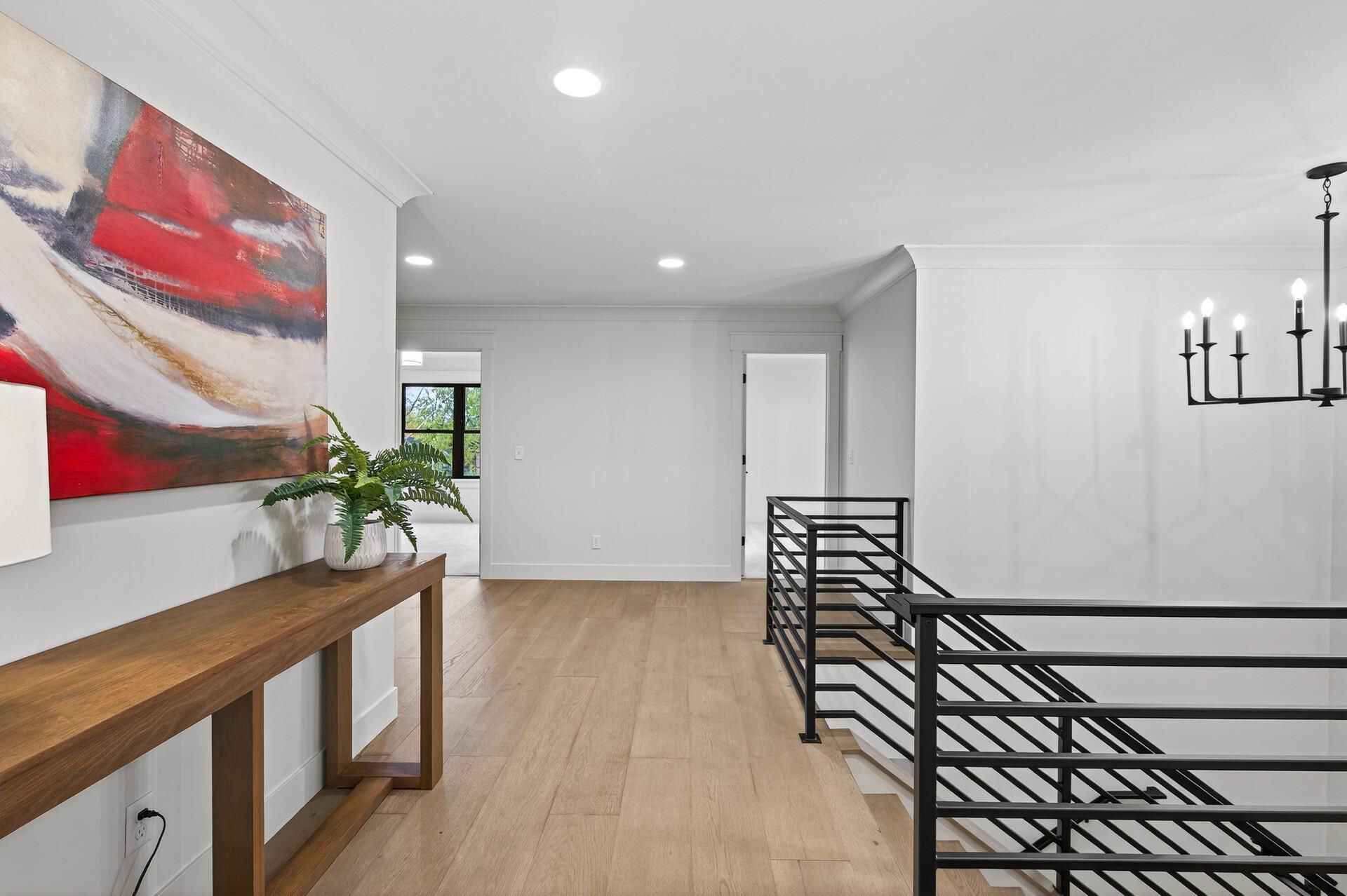 Upstairs landing with a black stair railing, wood floors, and a console table beneath abstract art