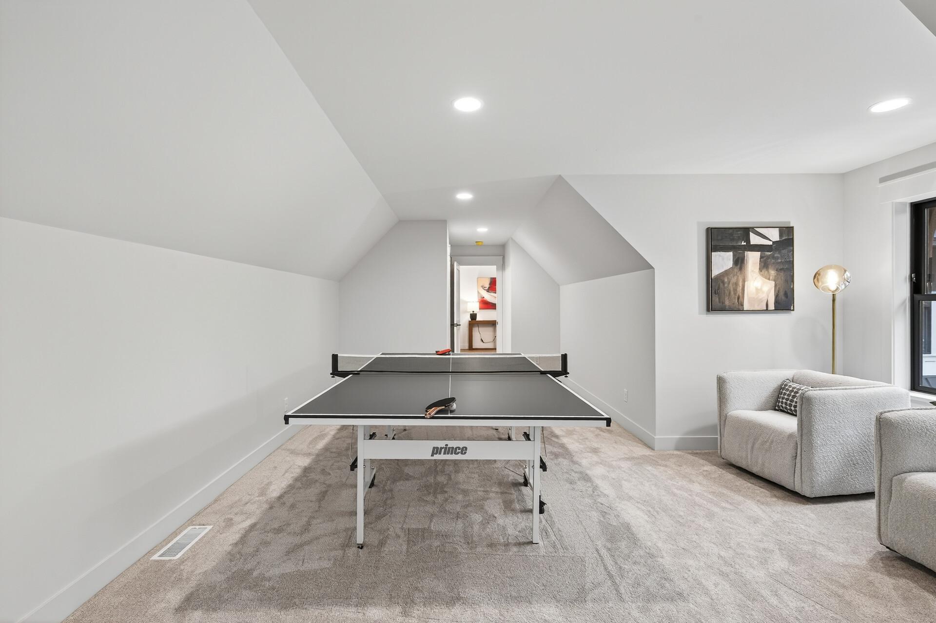 Furnished recreation room with a ping-pong table, paddles, and a light-colored armchair.