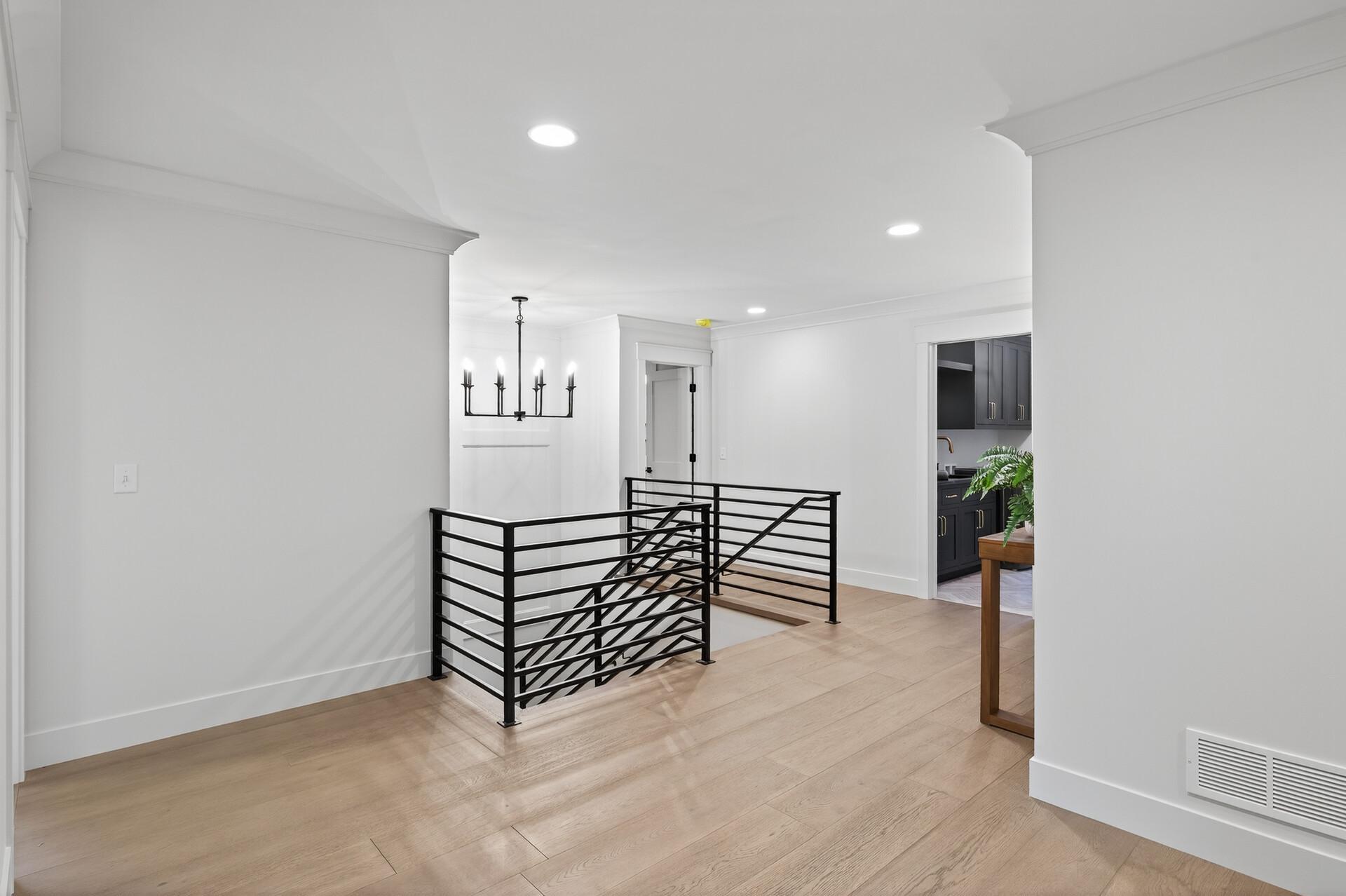 Upper-floor landing with pale wood floors, black stair railing, and a glimpse of dark kitchen cabinetry.