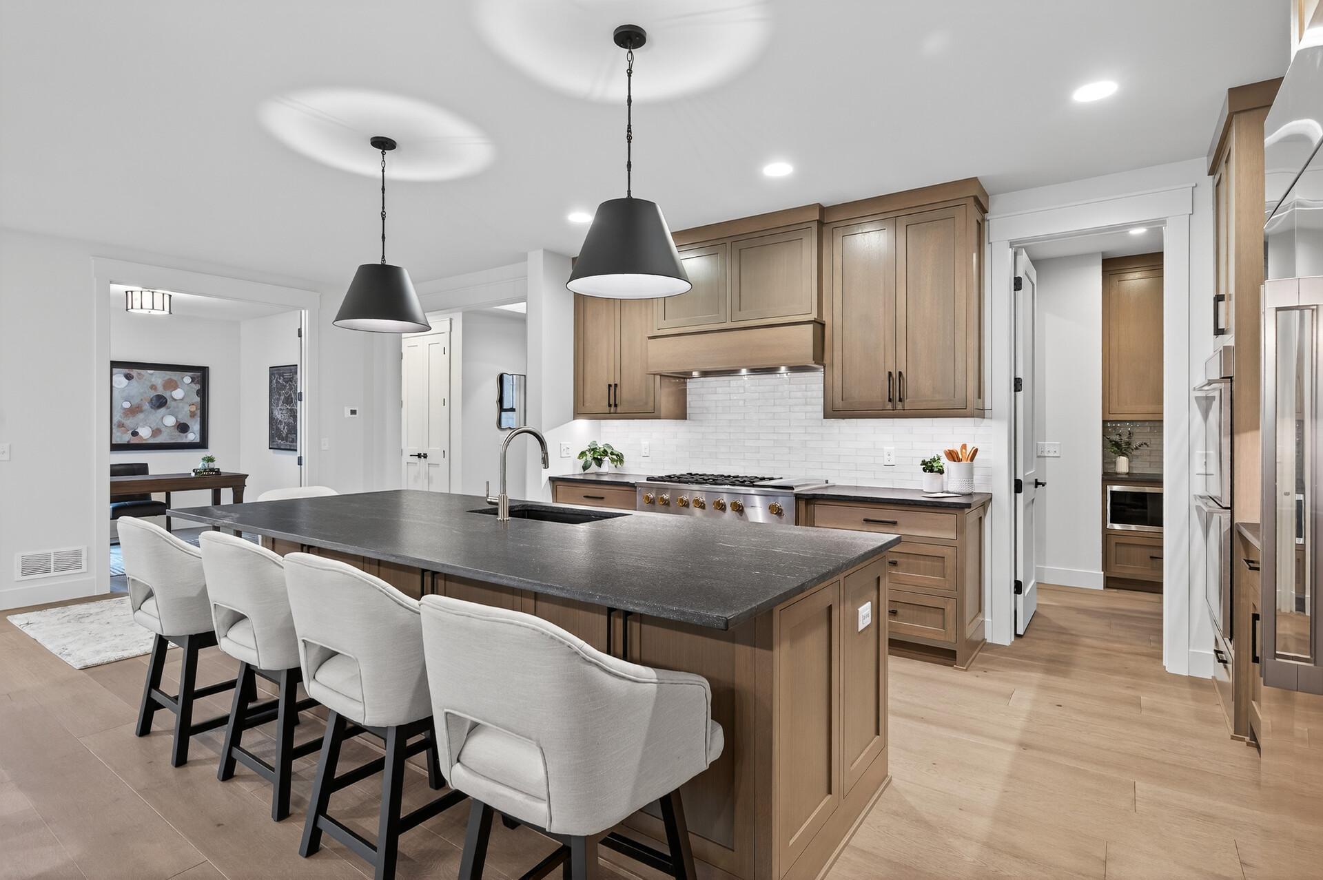 Kitchen with a large dark stone island, warm wood cabinets, and white upholstered bar stools.