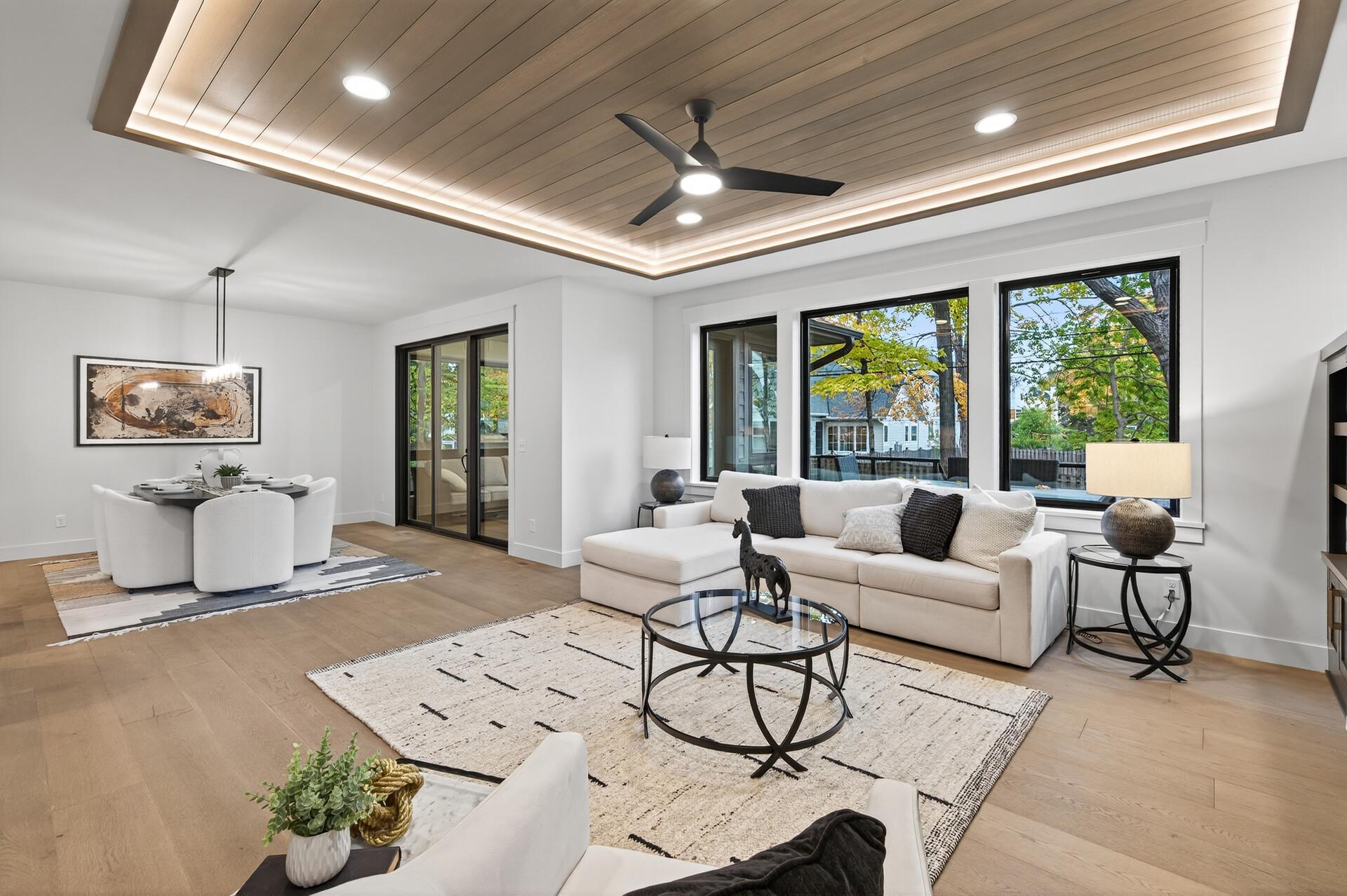 Living and dining room with a wood-paneled tray ceiling, white sectional, and large windows.