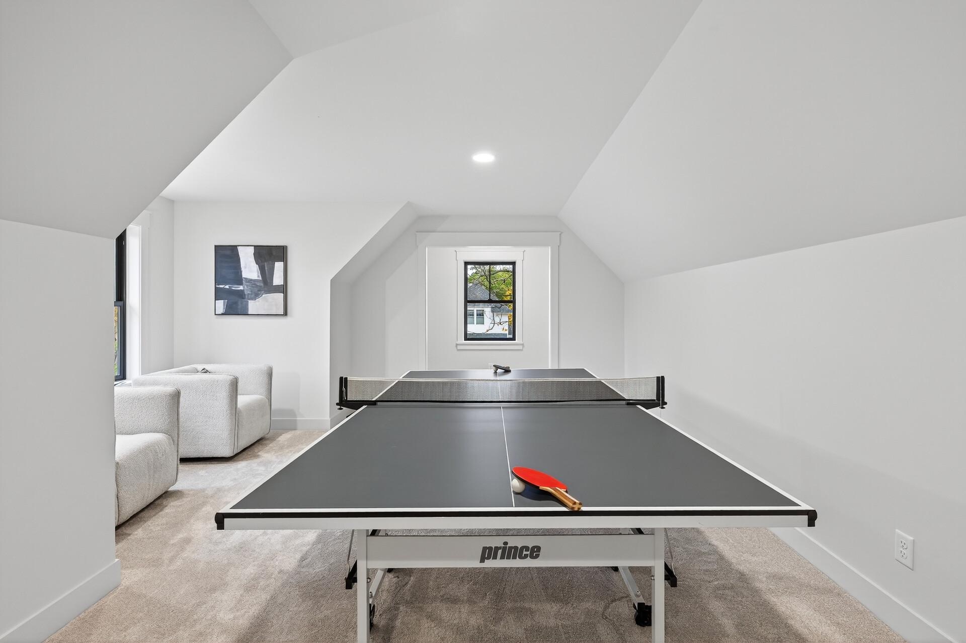 Attic recreation room with a ping-pong table and white sofa beneath sloped ceilings.