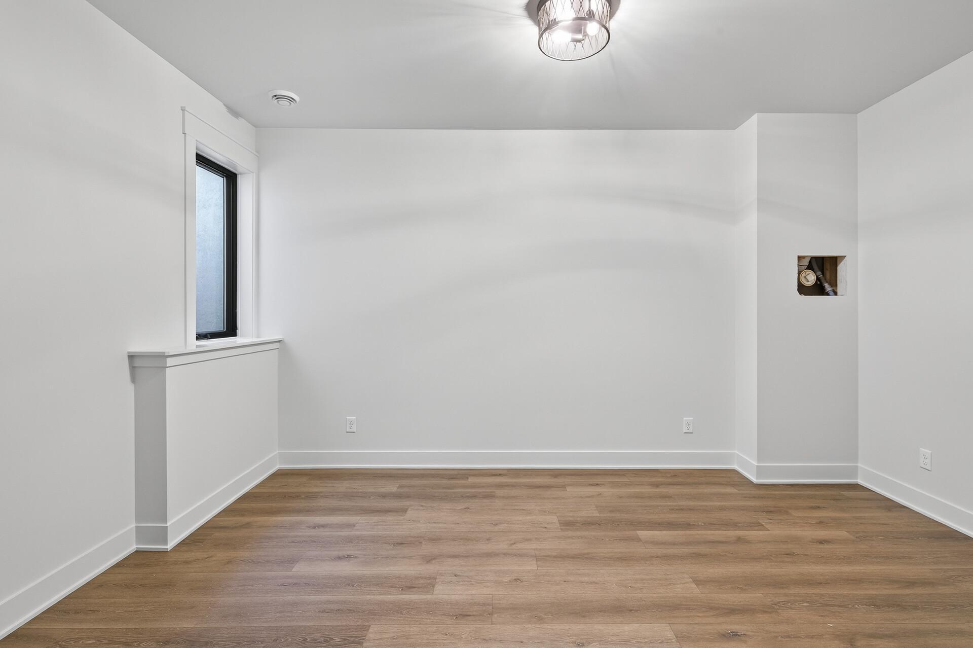 Empty room with brown plank flooring, a narrow window, and an exposed plumbing access opening.