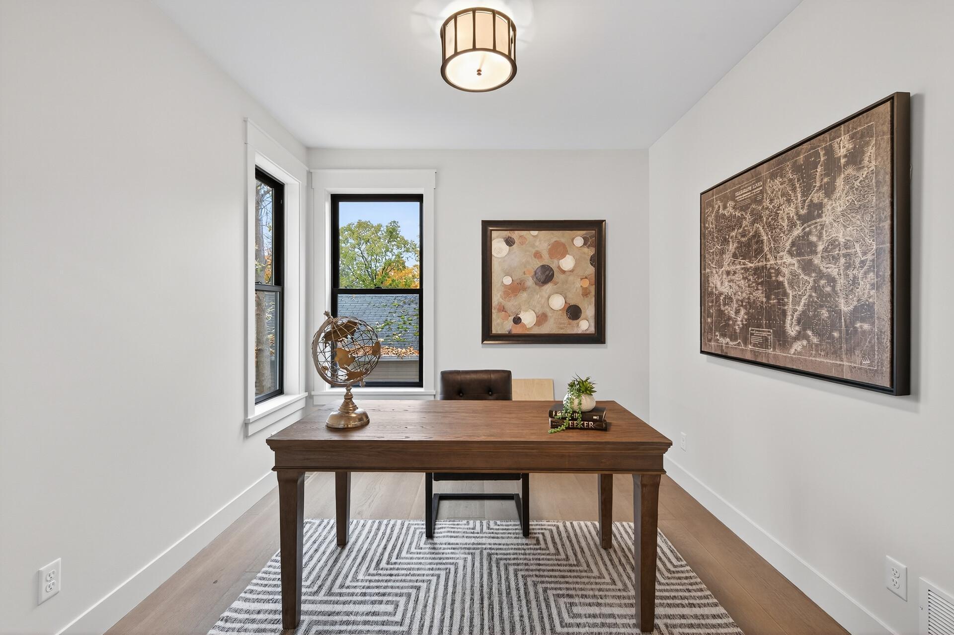 Staged home office with a dark wood desk, geometric rug, and large windows.