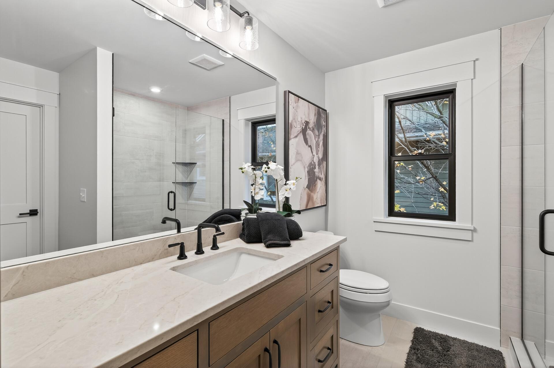 Updated bathroom with a wood vanity, pale stone counter, and glass-enclosed shower.