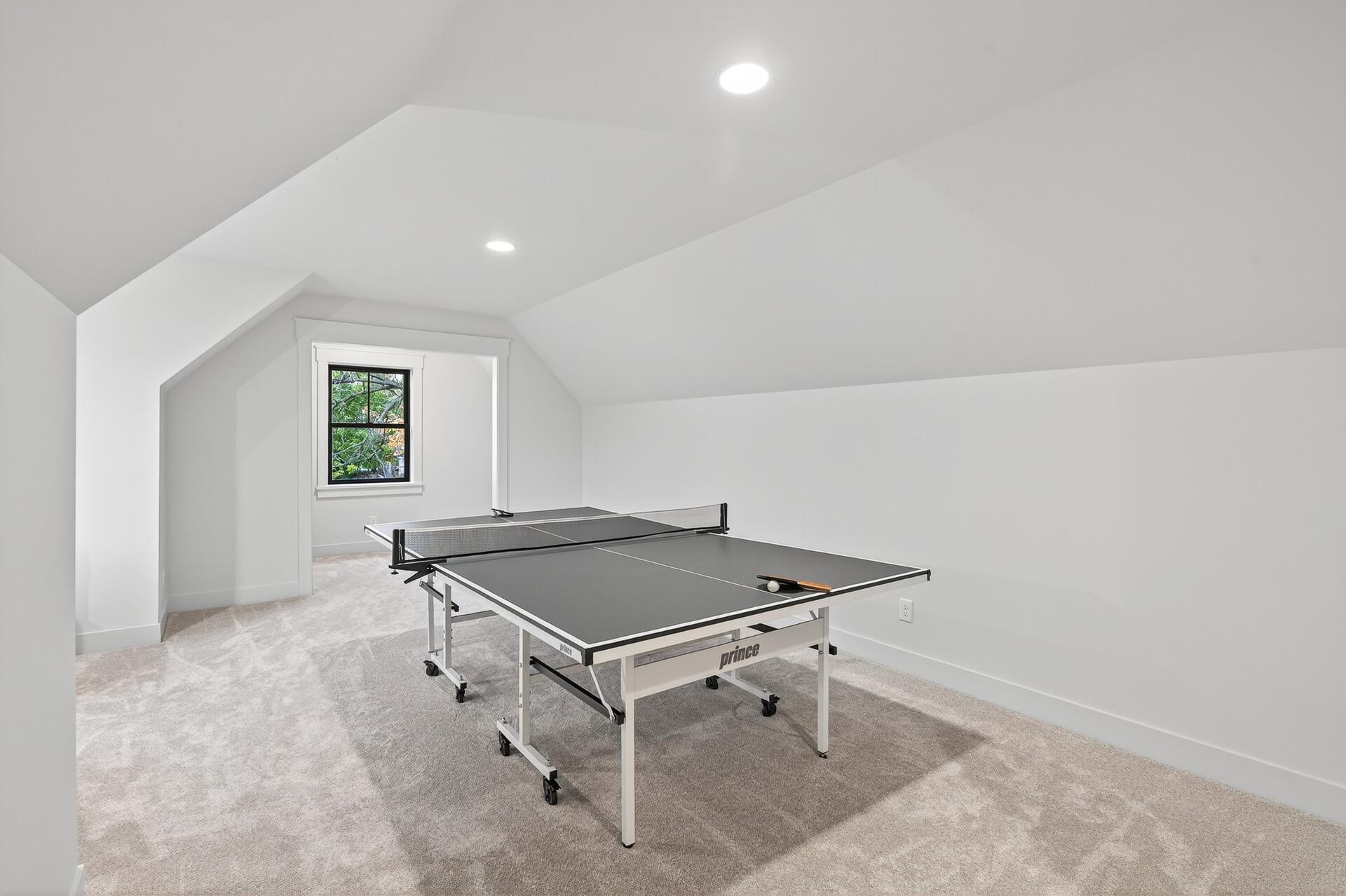 Game room with a ping-pong table beneath a sloped ceiling and beside a window.