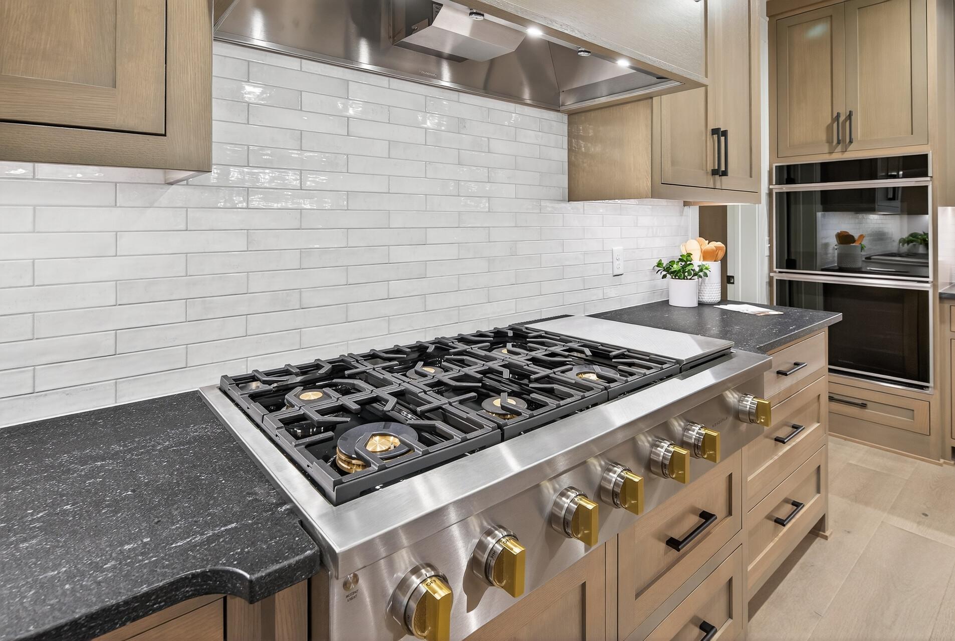 Kitchen with a large stainless steel gas range, dark counters, white tile backsplash, and built-in double ovens.