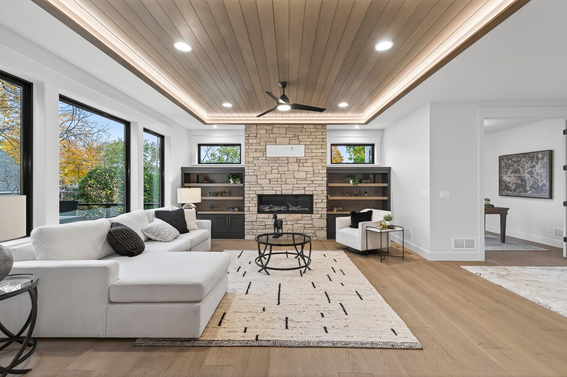 Living room with a stone fireplace, white sectional, built-in shelves, and wood-plank ceiling.