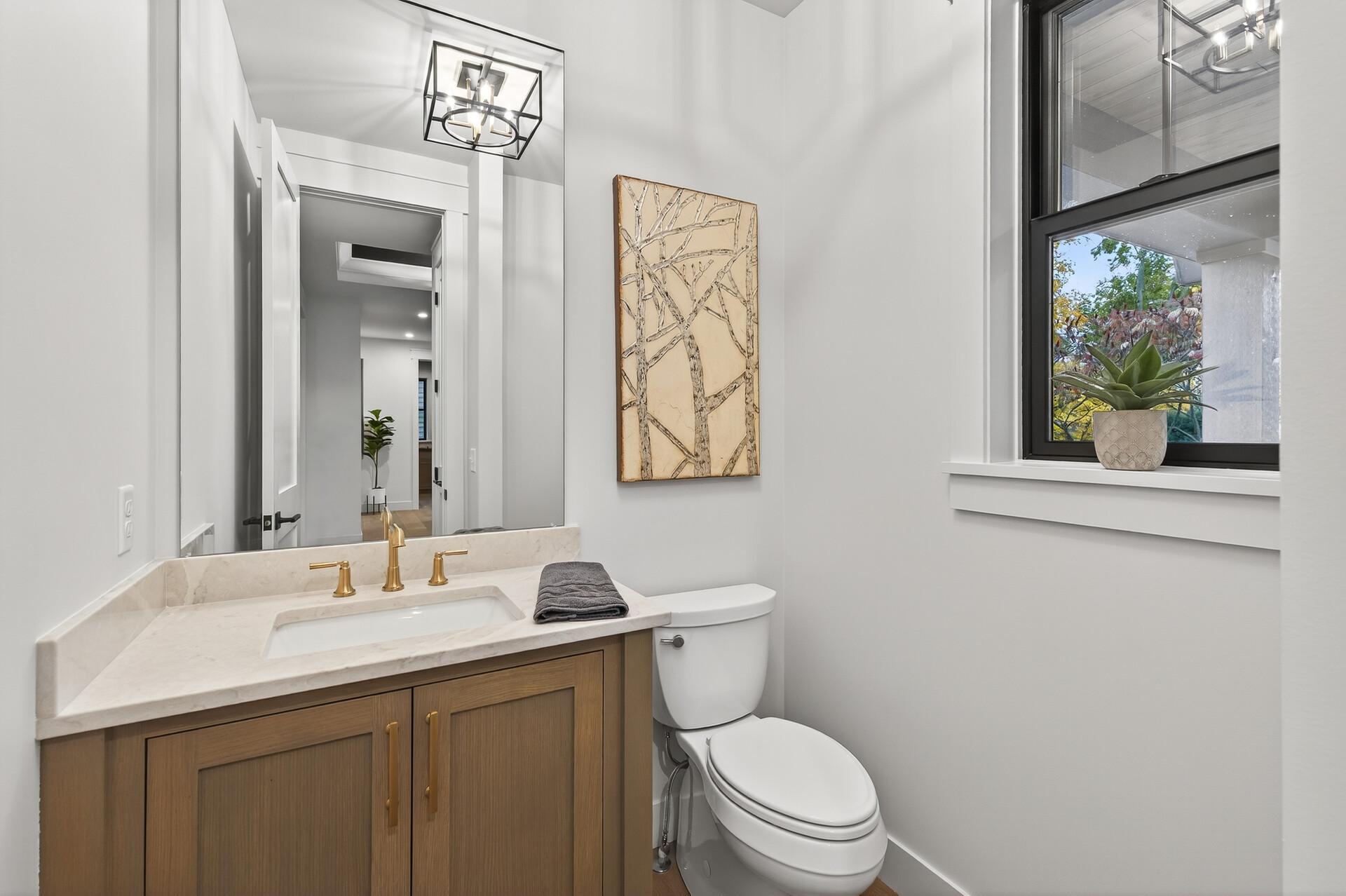 Bright bathroom with a wood vanity, gold faucet, and black-framed window overlooking autumn foliage.