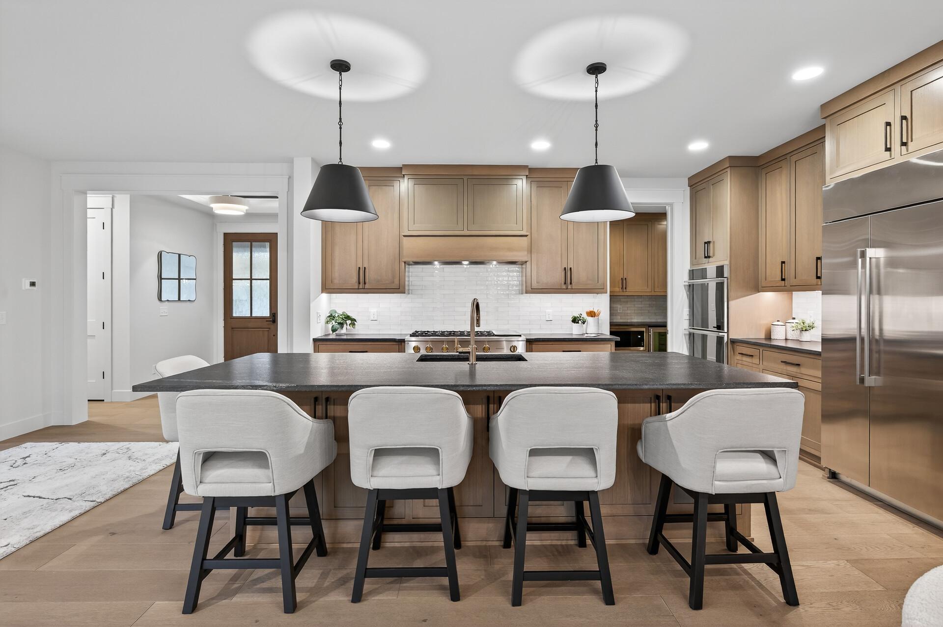 Kitchen with a large dark island and four white bar stools, light wood cabinets, and stainless steel appliances.