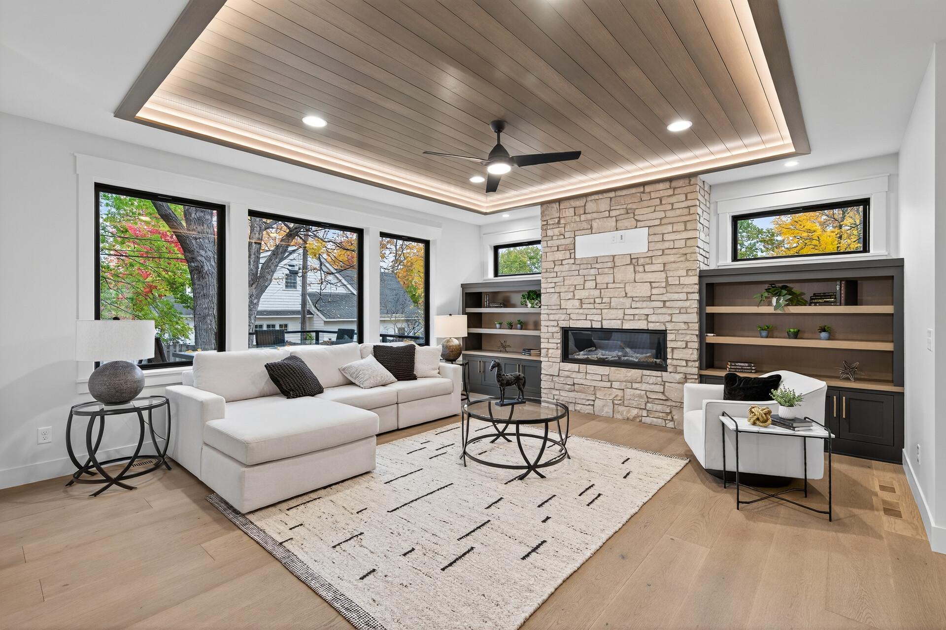 Living room with a stone fireplace, white sectional, and illuminated wood tray ceiling.