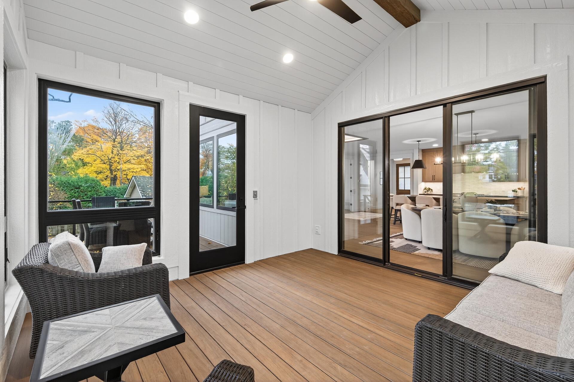 Covered porch with wicker seating, wood-plank flooring, and views of autumn trees.