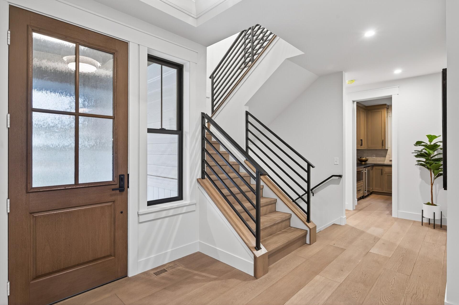 Entry foyer with a wood front door and light wood staircase with black railings.
