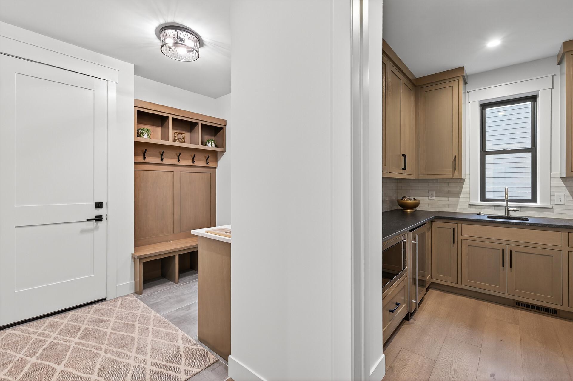 Kitchen with warm wood cabinets and dark counters beside a mudroom with built-in cubbies and bench.