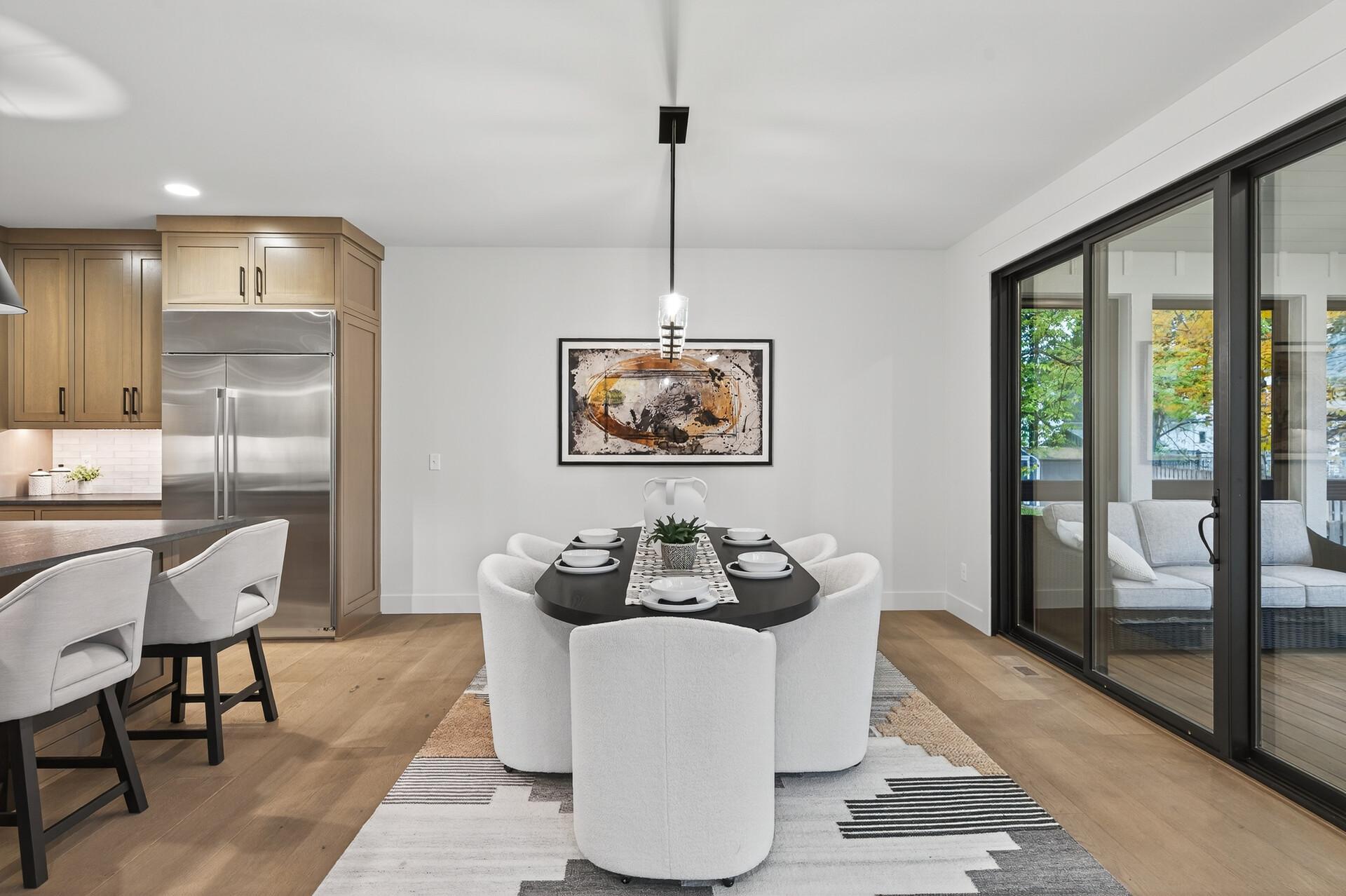 Dining room with a dark table, white chairs, light wood kitchen cabinetry, and sliding glass doors.