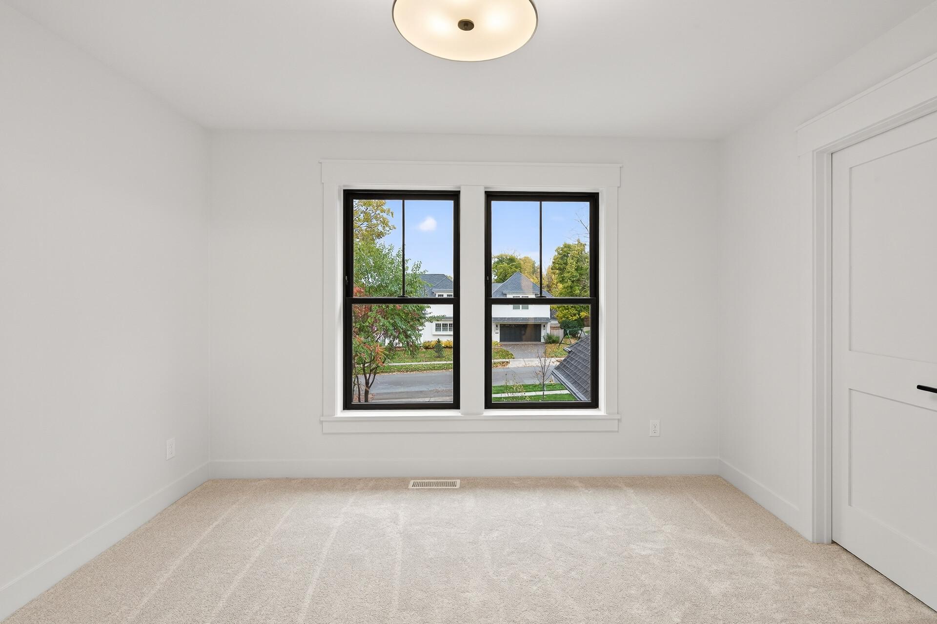 Empty carpeted room with two black-framed windows overlooking neighboring homes.