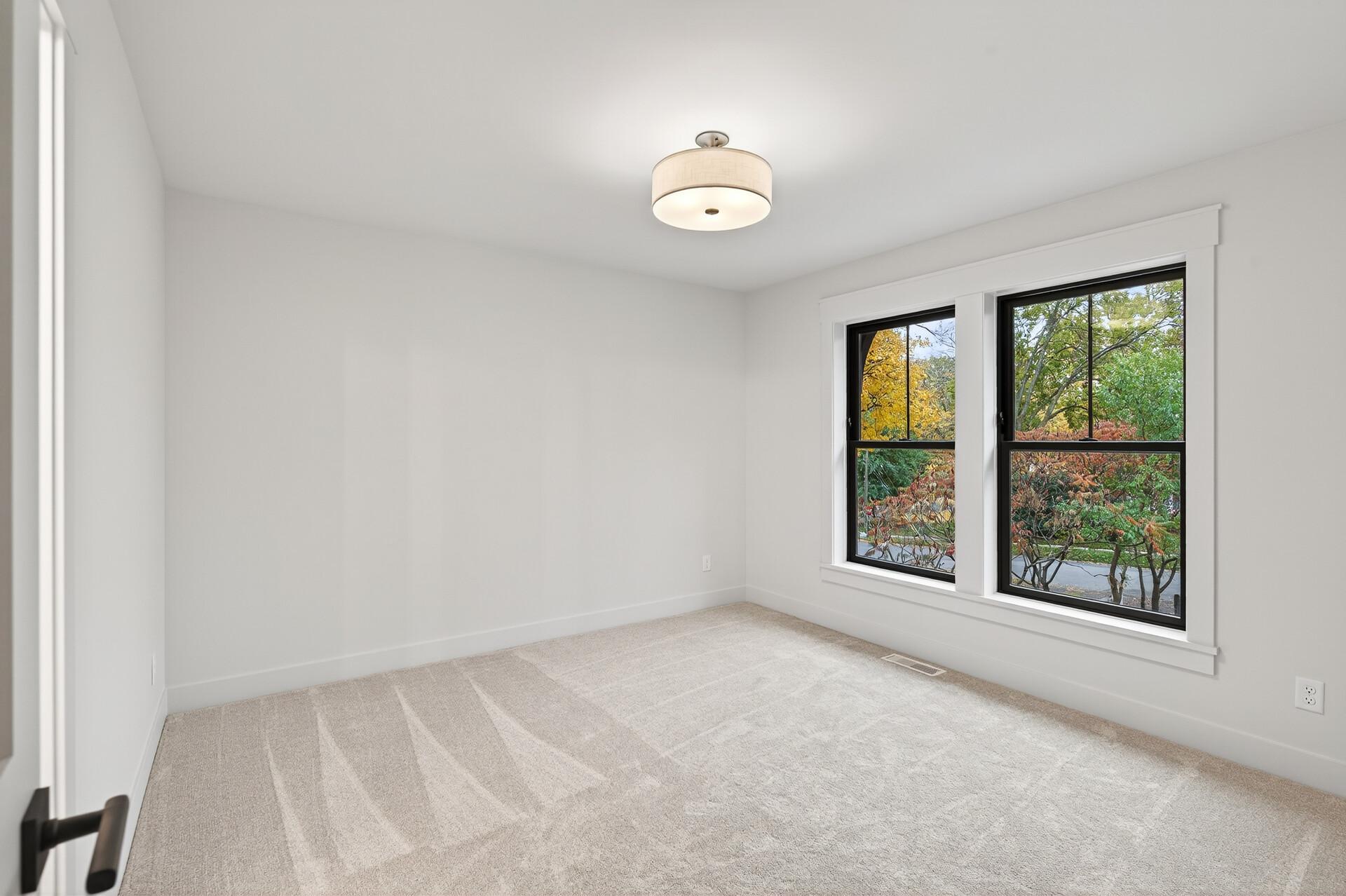 Vacant carpeted room with two large windows overlooking autumn trees