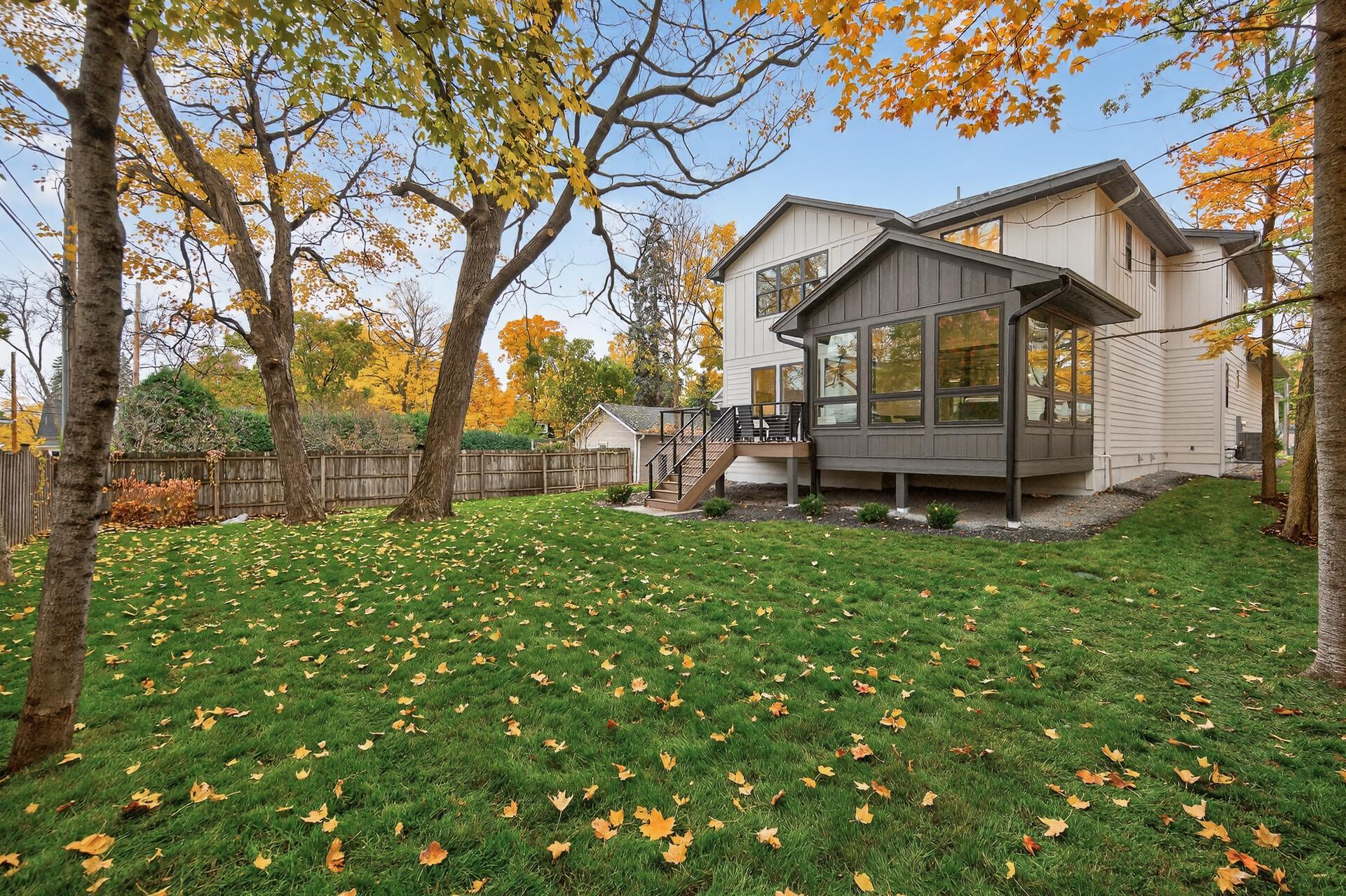 White two-story house with a dark enclosed porch and raised deck beyond a leaf-strewn lawn.