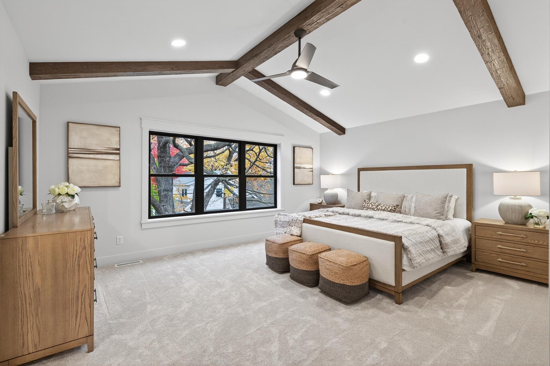 Staged bedroom with exposed wood ceiling beams, a large window, and a wood-framed bed.