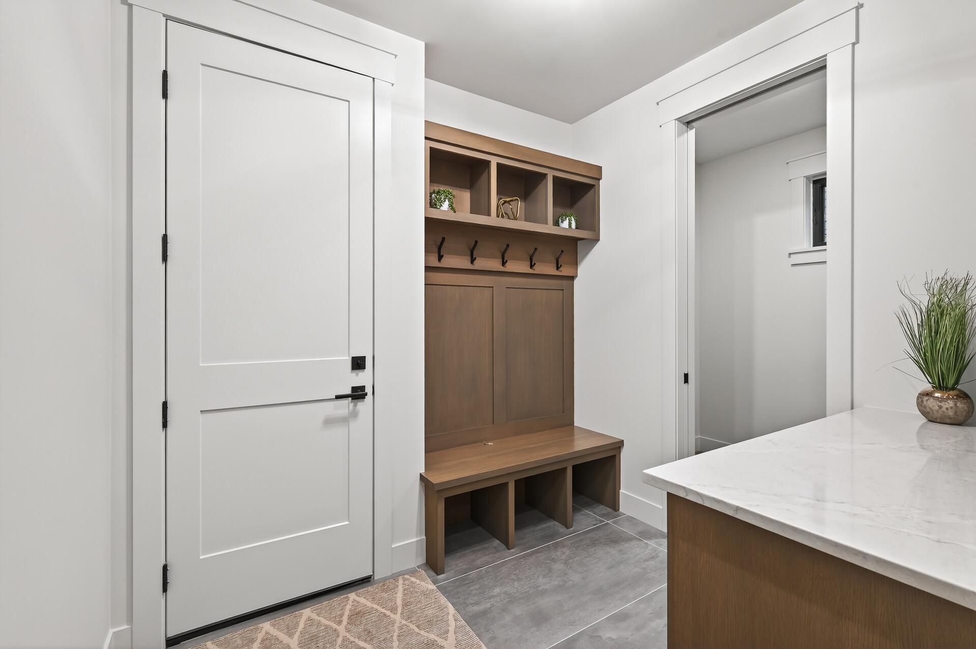 Mudroom with a walnut built-in bench, cubbies, coat hooks, and white stone countertop.