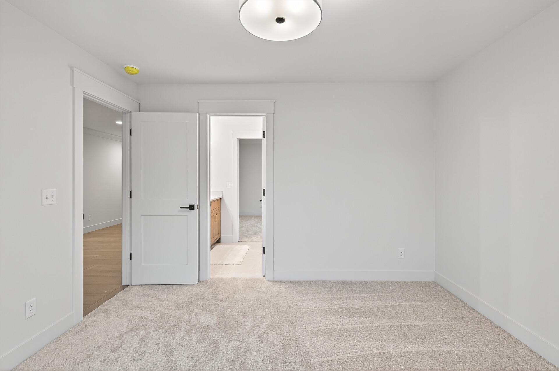 Vacant bedroom with light carpet, white walls, and open doors to adjoining rooms.