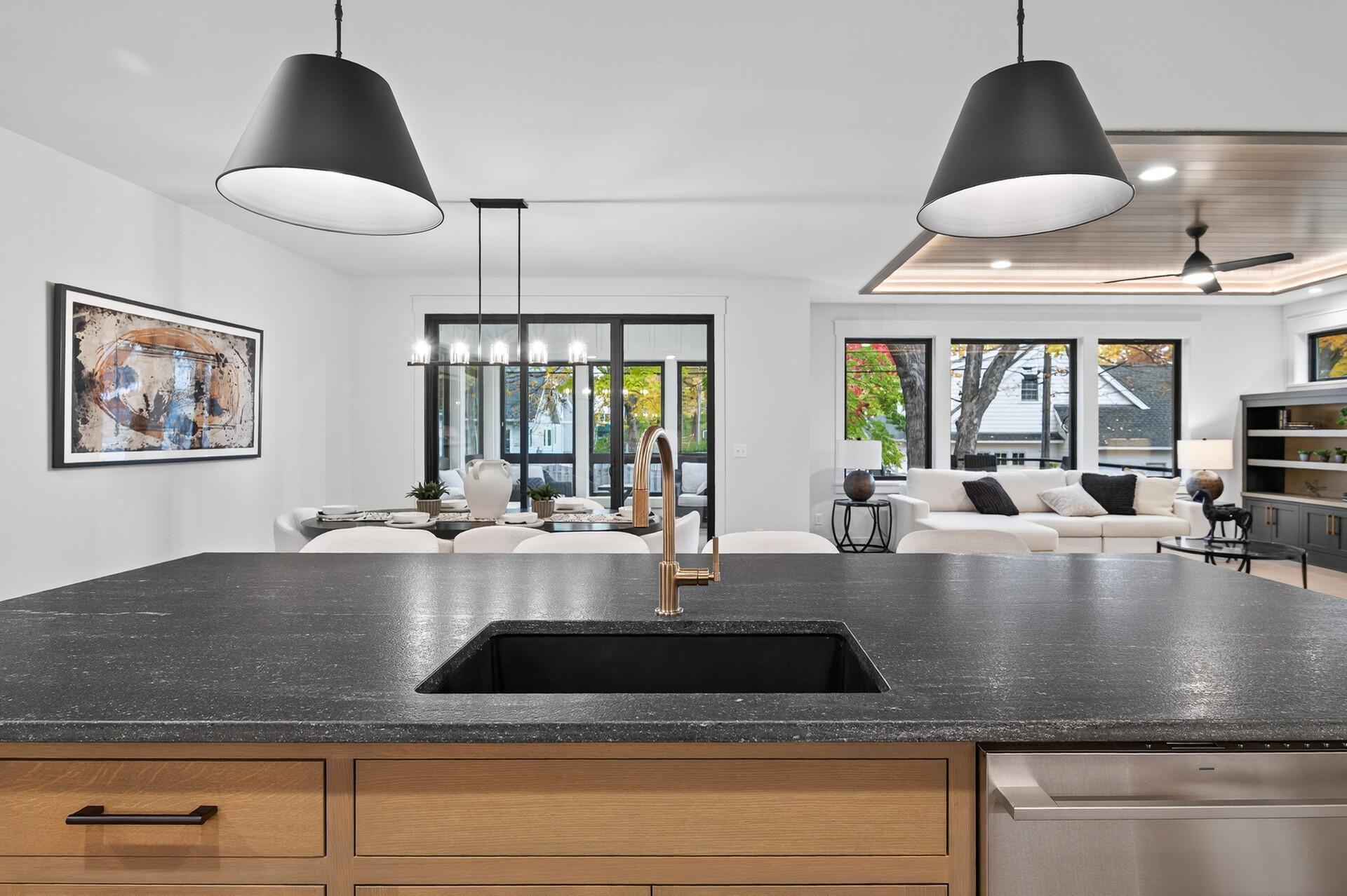 Open-plan kitchen with dark stone island, brass faucet, and dining and living areas beyond.
