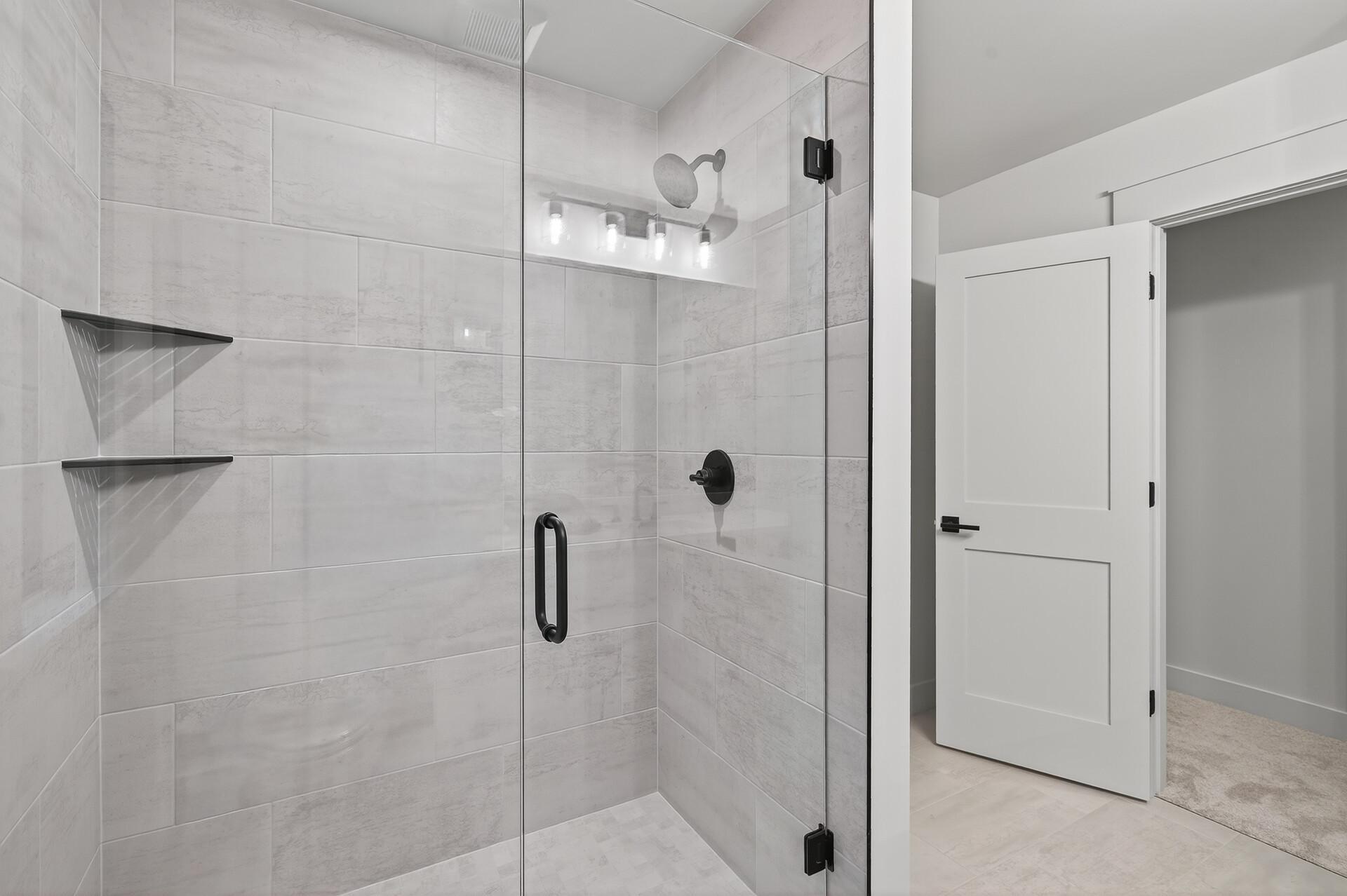 Walk-in shower with light gray tile, glass enclosure, and matte black fixtures.