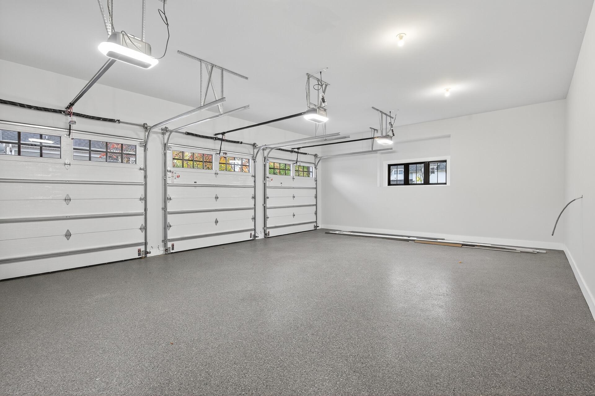 Empty three-car garage with three white doors and a wide gray speckled floor.
