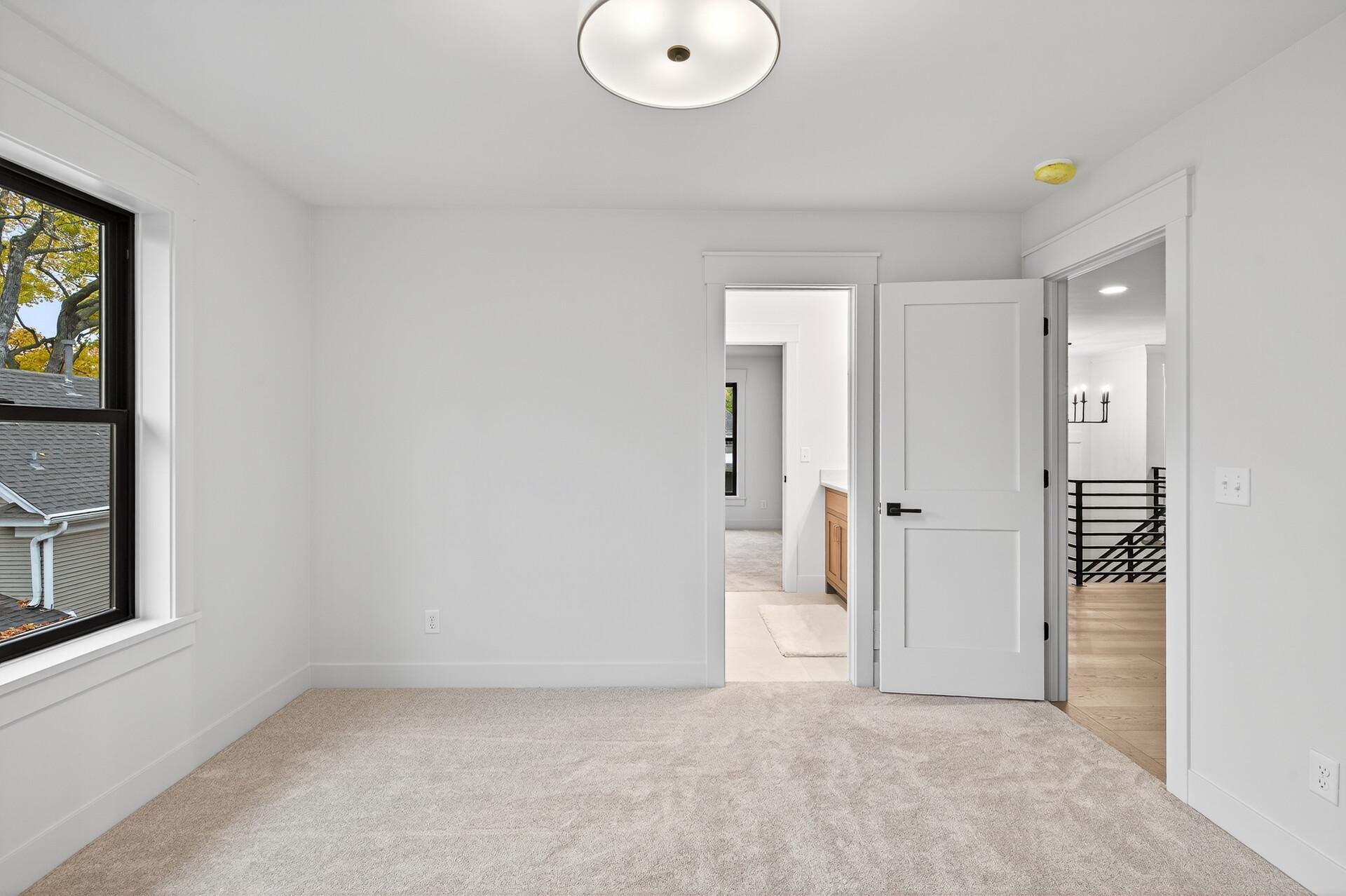 Vacant carpeted bedroom with a black-framed window and open doors to adjoining rooms.