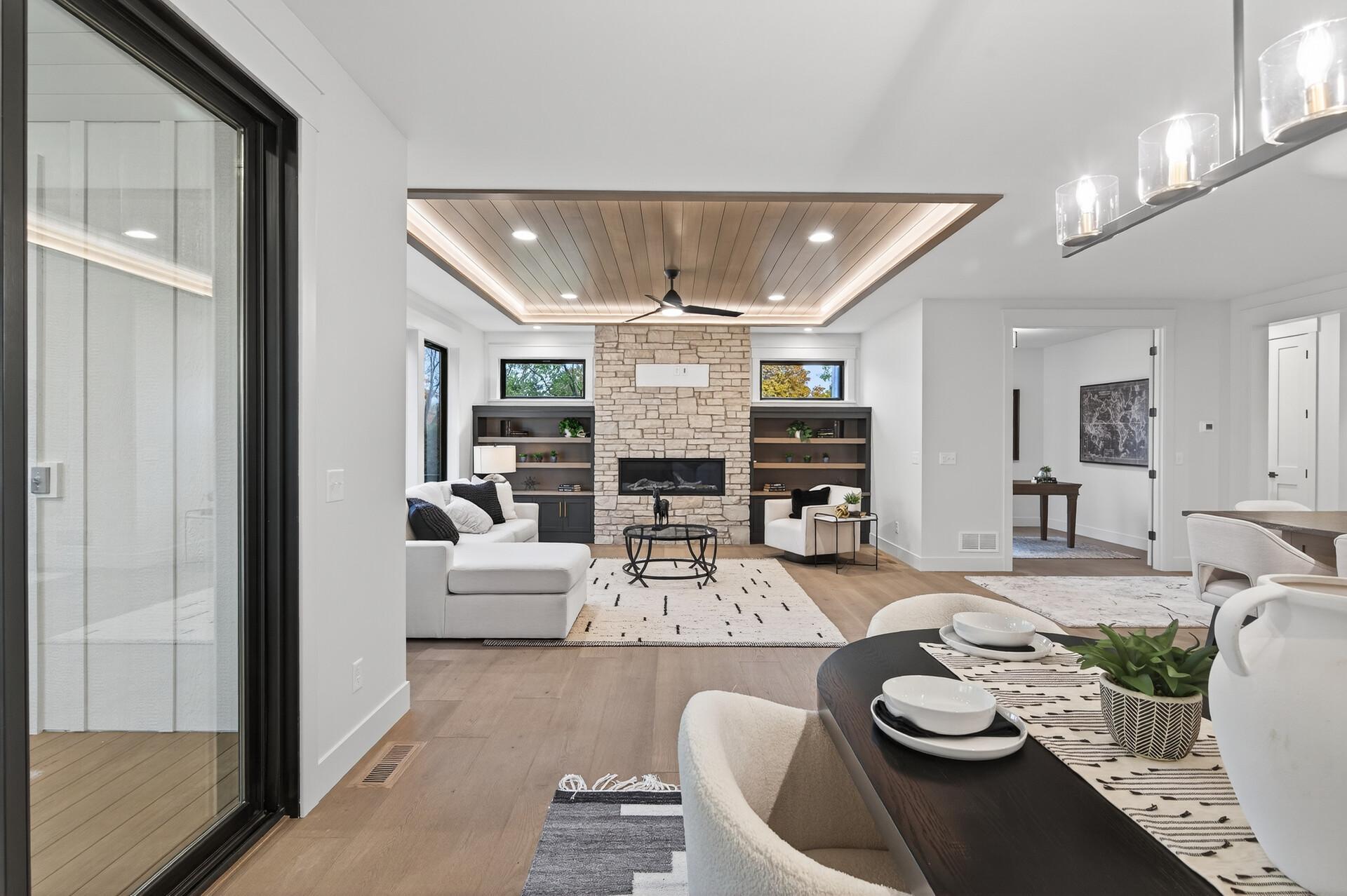 Open-plan living and dining room with a stone fireplace, built-in shelves, and a recessed wood ceiling.