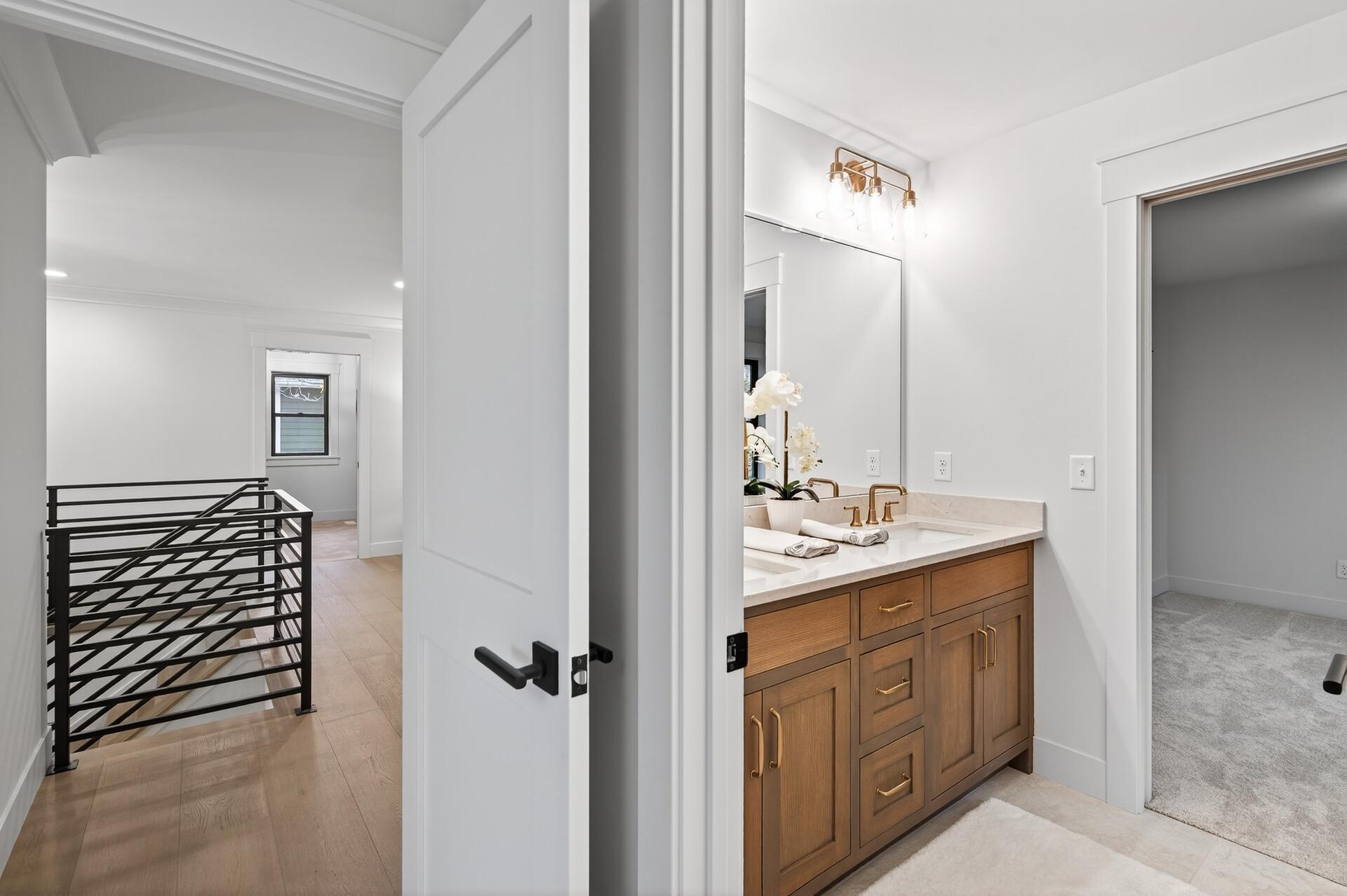 Bathroom with a wood vanity, brass faucets, and a large mirror beside a landing with black metal railing.