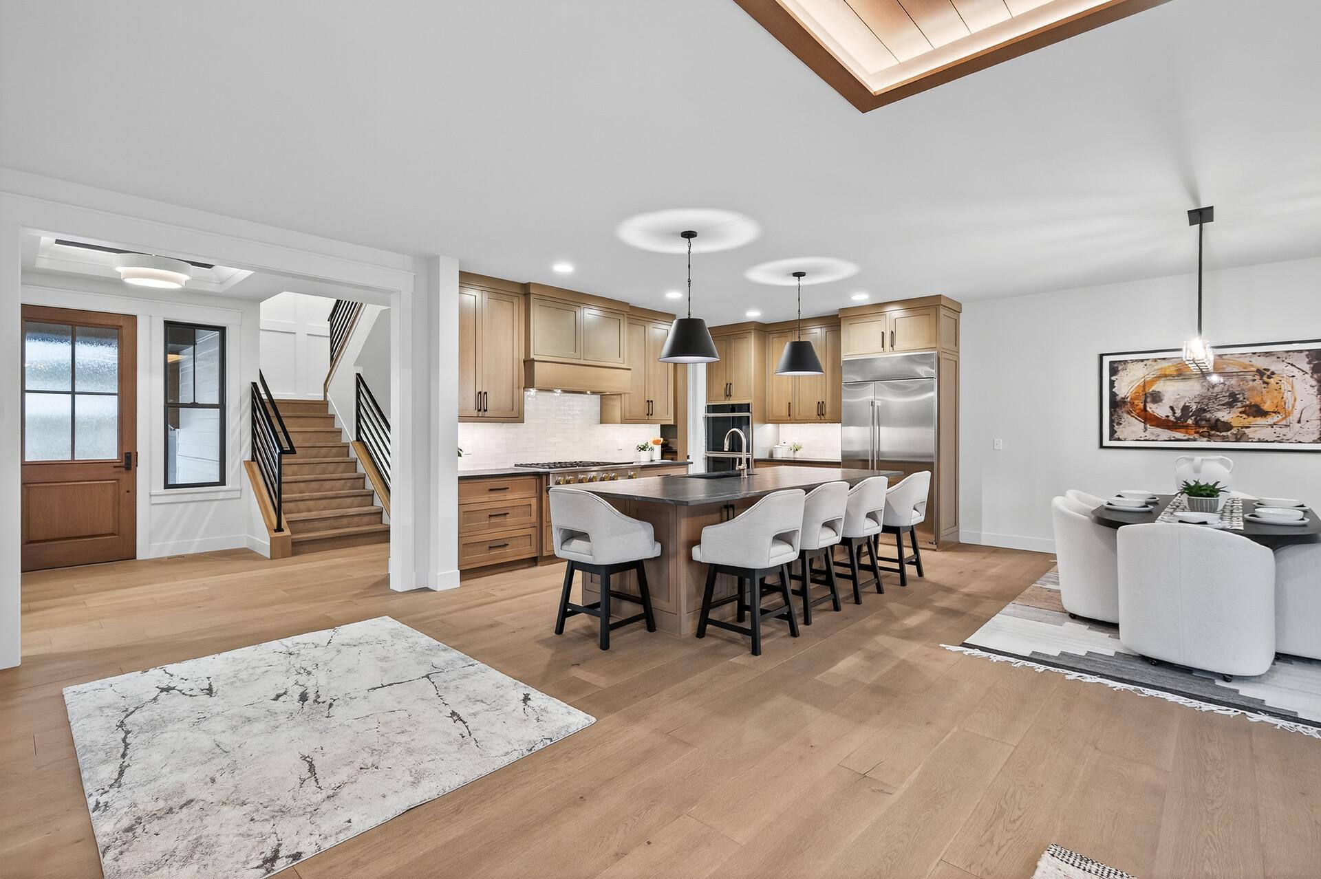 Open kitchen and dining area with a wood-cabinet island, stainless steel appliances, and staircase.