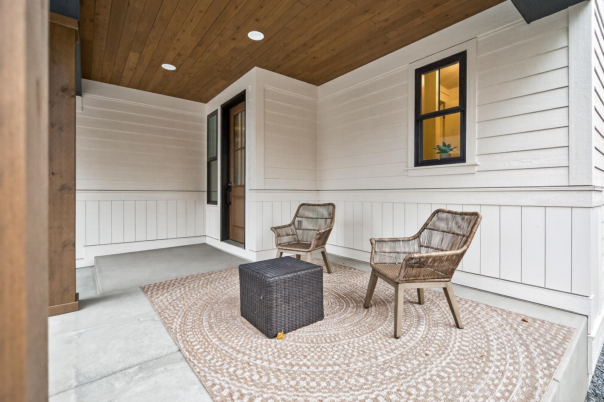 Covered porch with a wood ceiling, wicker chairs, and a woven rug.