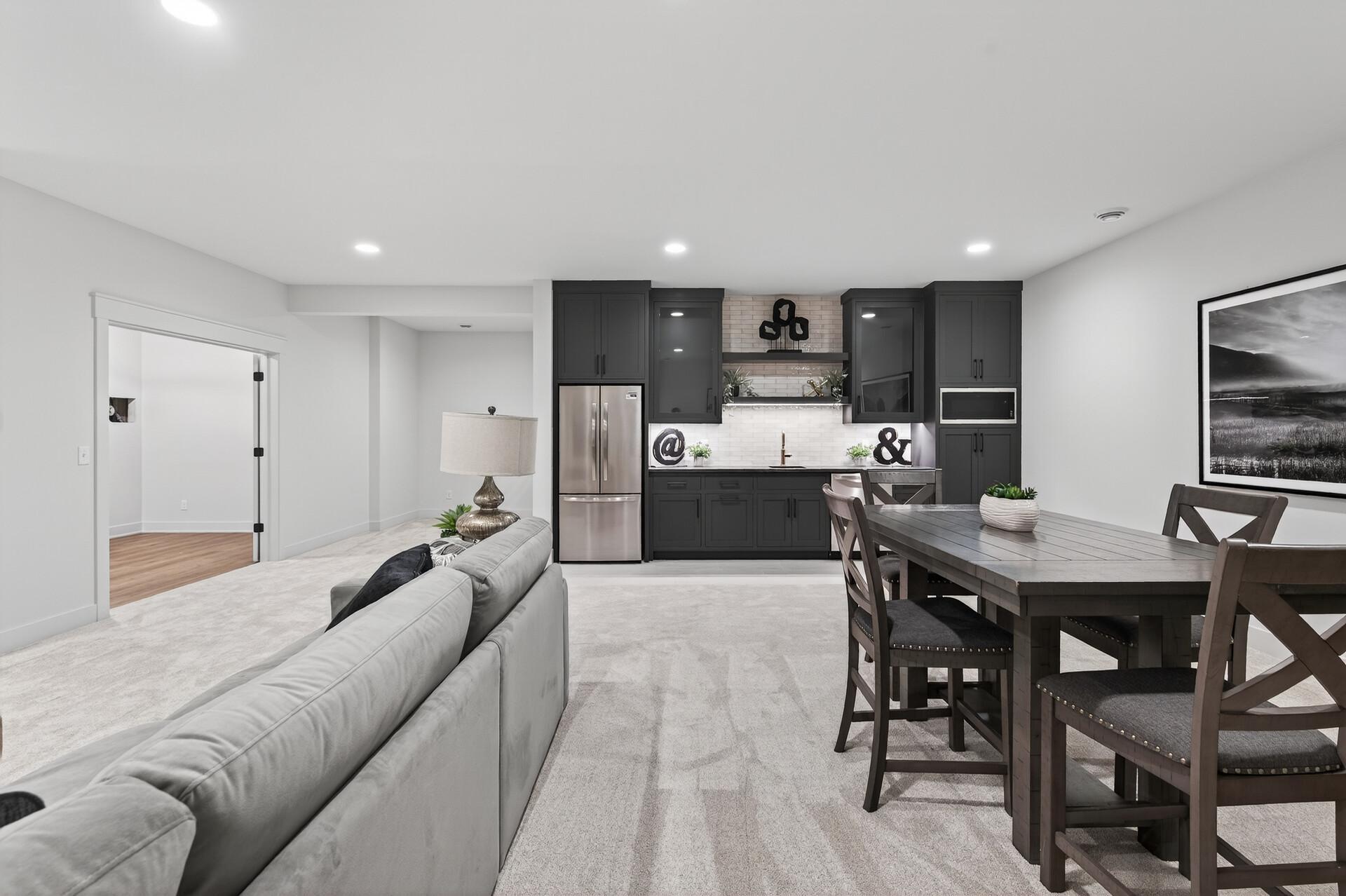 Open-plan living and dining area with charcoal kitchen cabinets, stainless appliances, and a dark wood table.