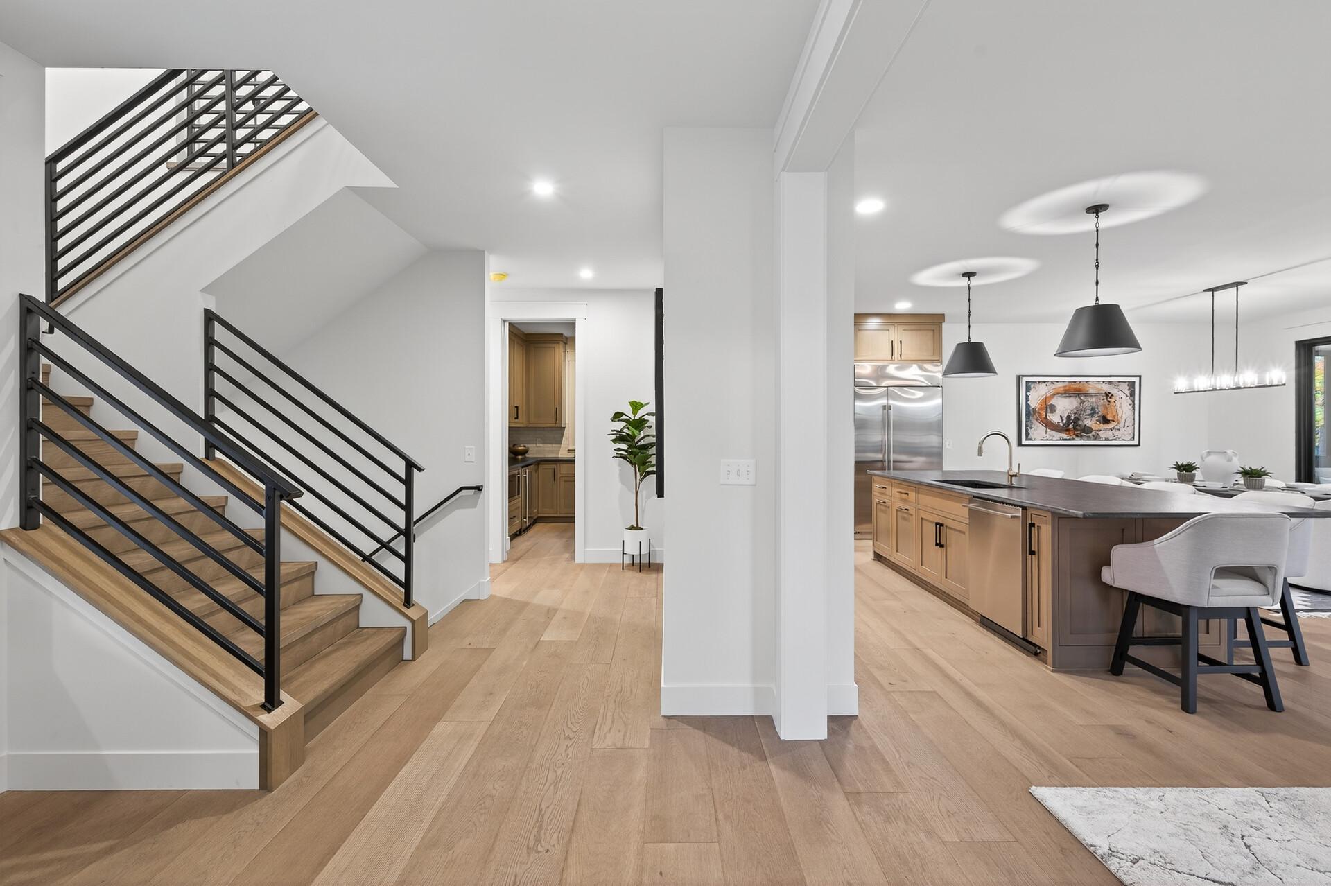 Open-plan kitchen and staircase with a large island, wood flooring, and black metal railings.