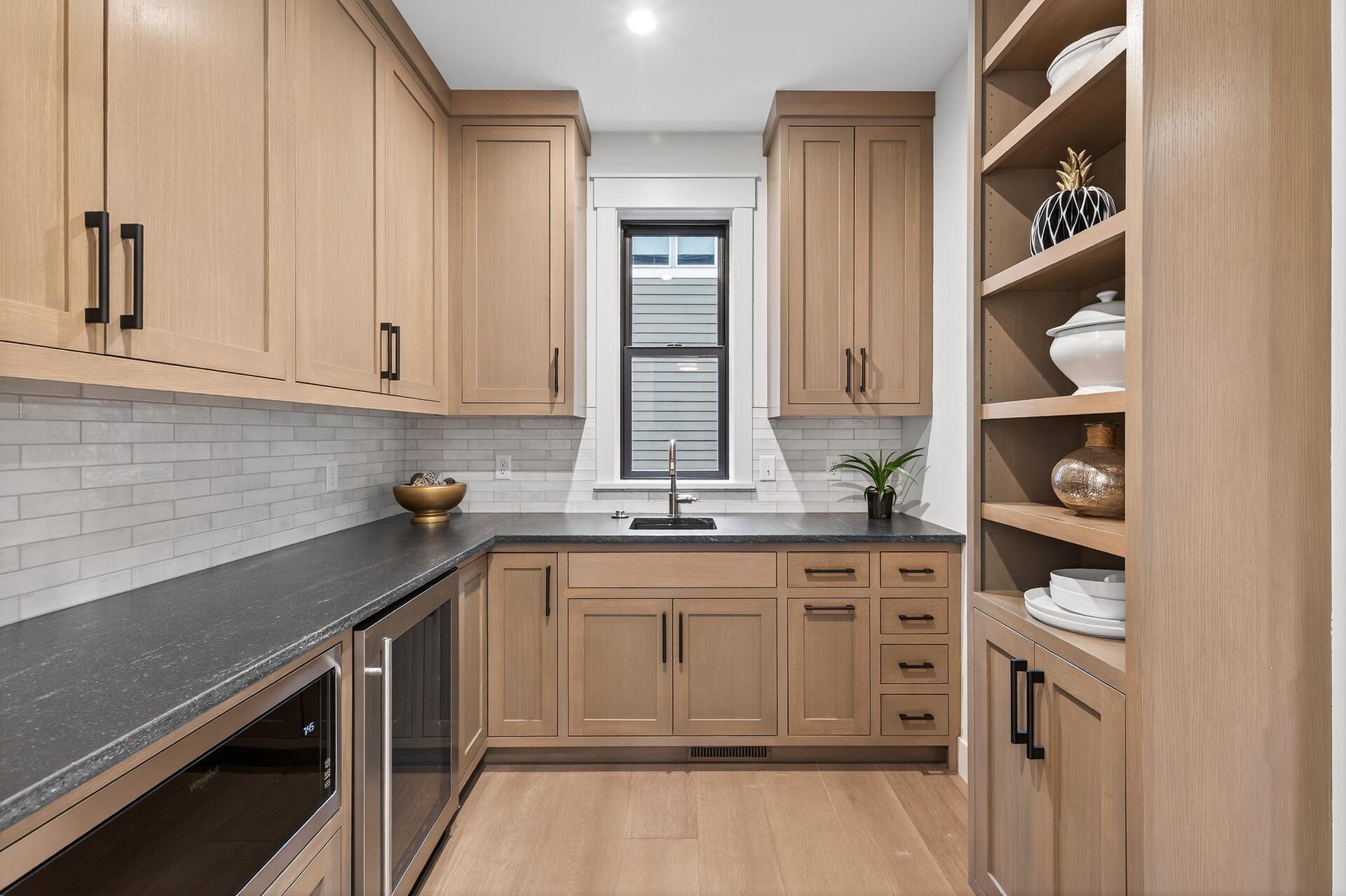 Kitchen with light wood cabinets, dark countertops, subway tile backsplash, and open dish shelves.