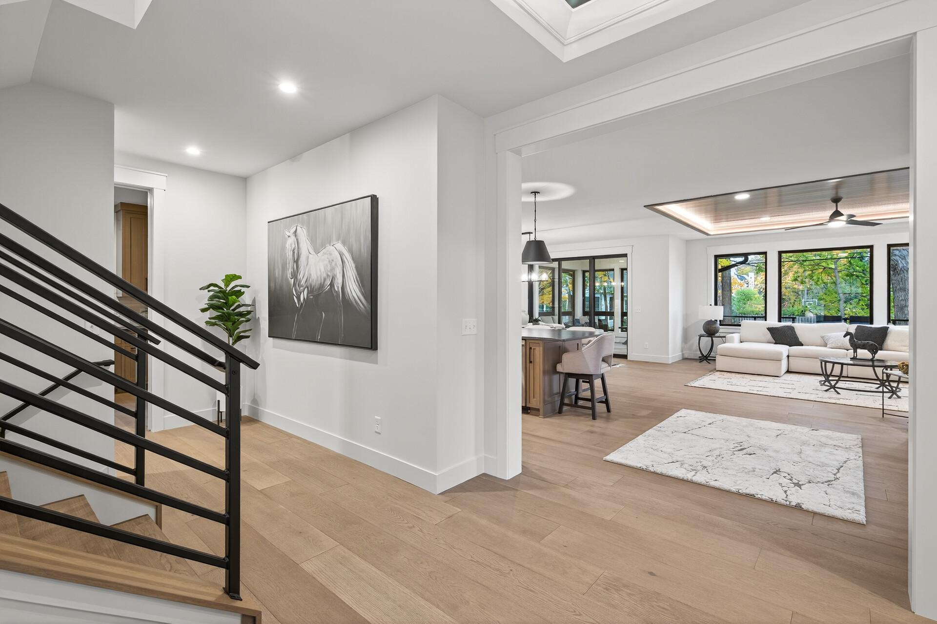 Open entry with black-railed staircase overlooking a bright living room with large windows.
