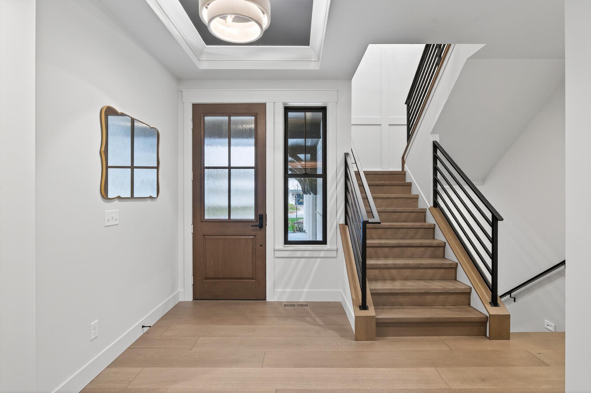 Entry foyer with a wood staircase, black metal railings, and a glass-paneled front door.