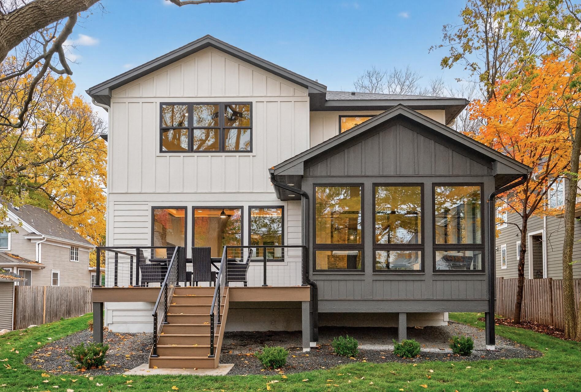 Rear of a white two-story home with a raised deck, black railings, and autumn trees.